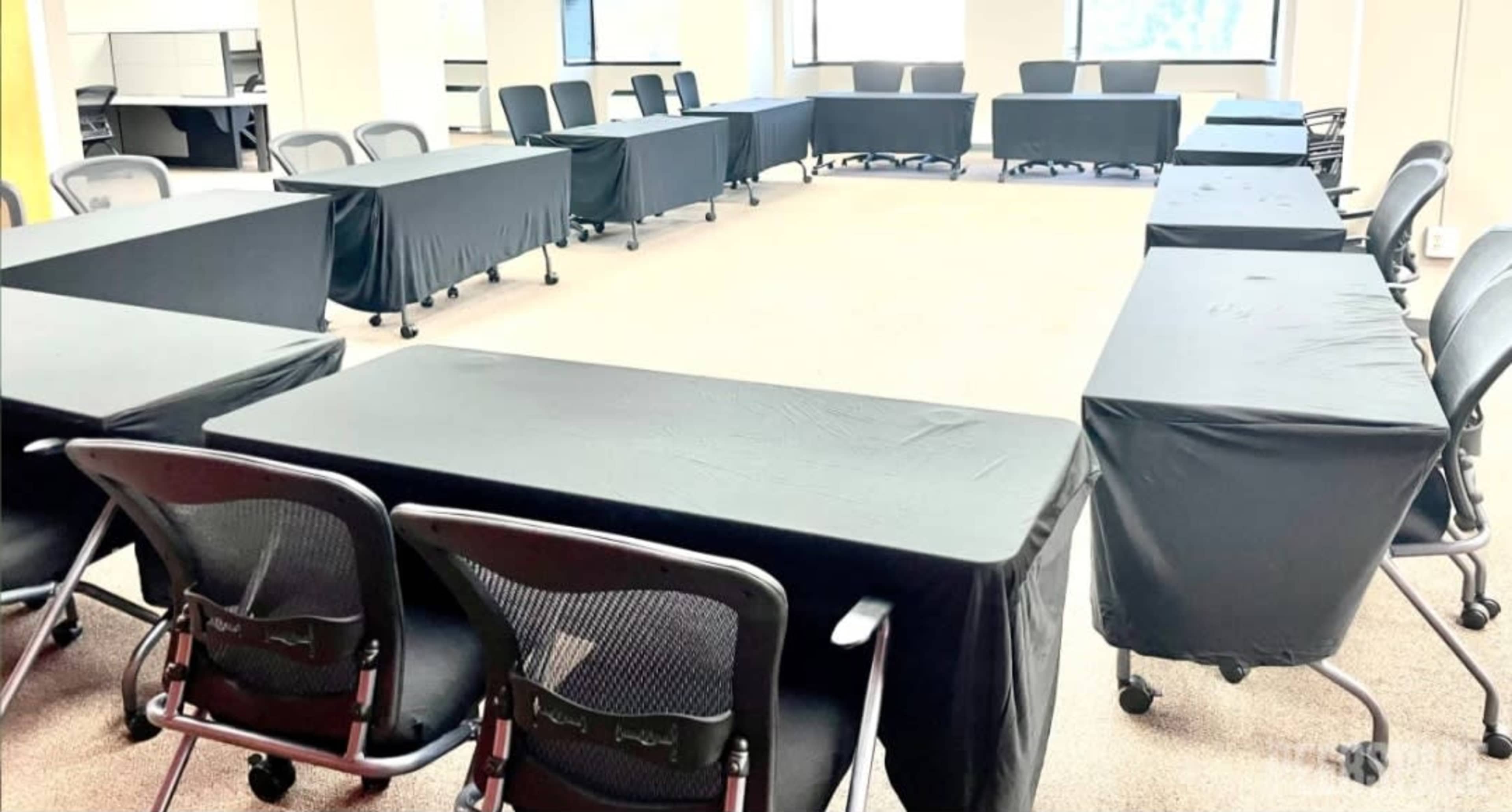 A conference room arranged with multiple tables covered in black cloth, surrounded by chairs.