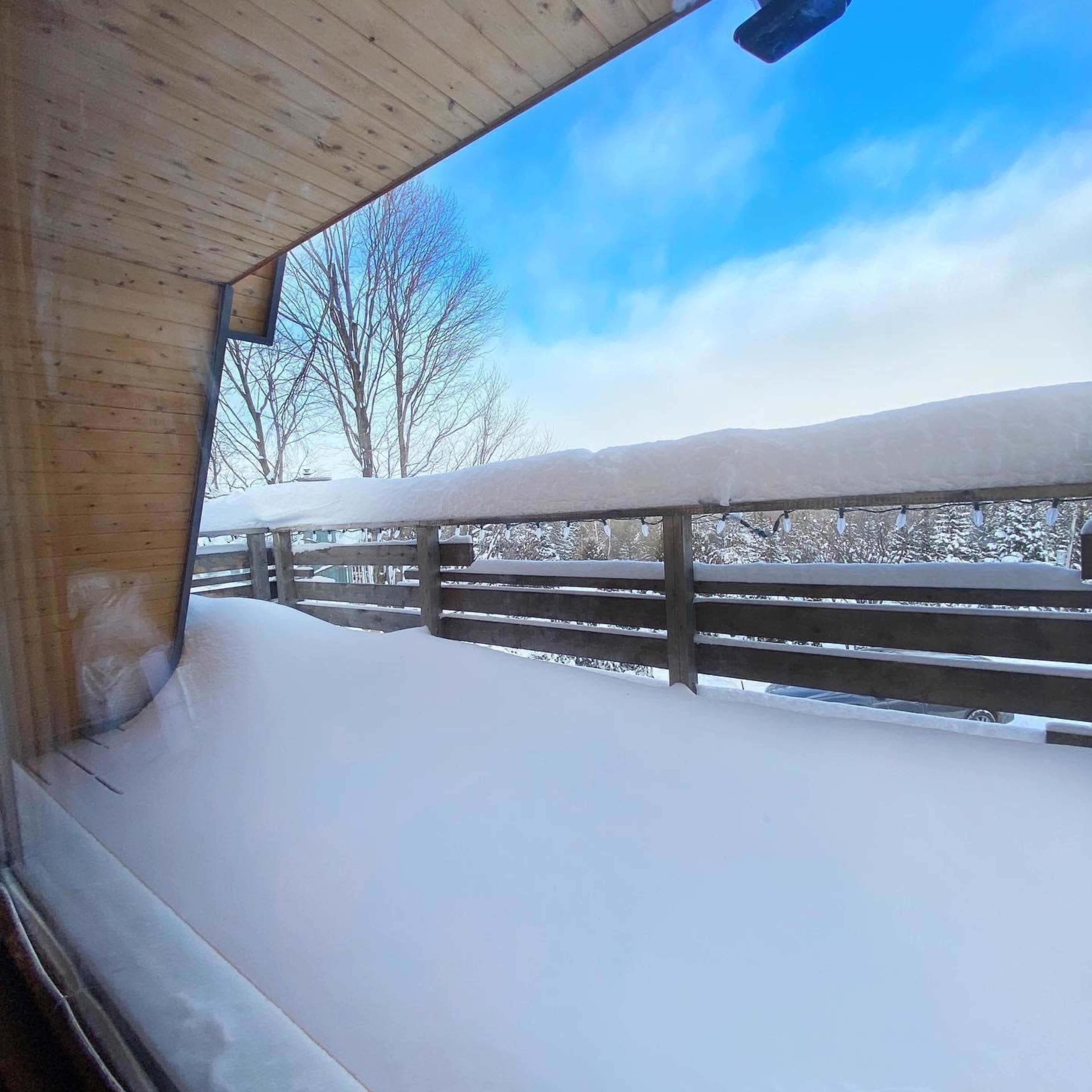 The image shows a snowy outdoor scene viewed from a window, with snow covering the balcony and trees in the background.
