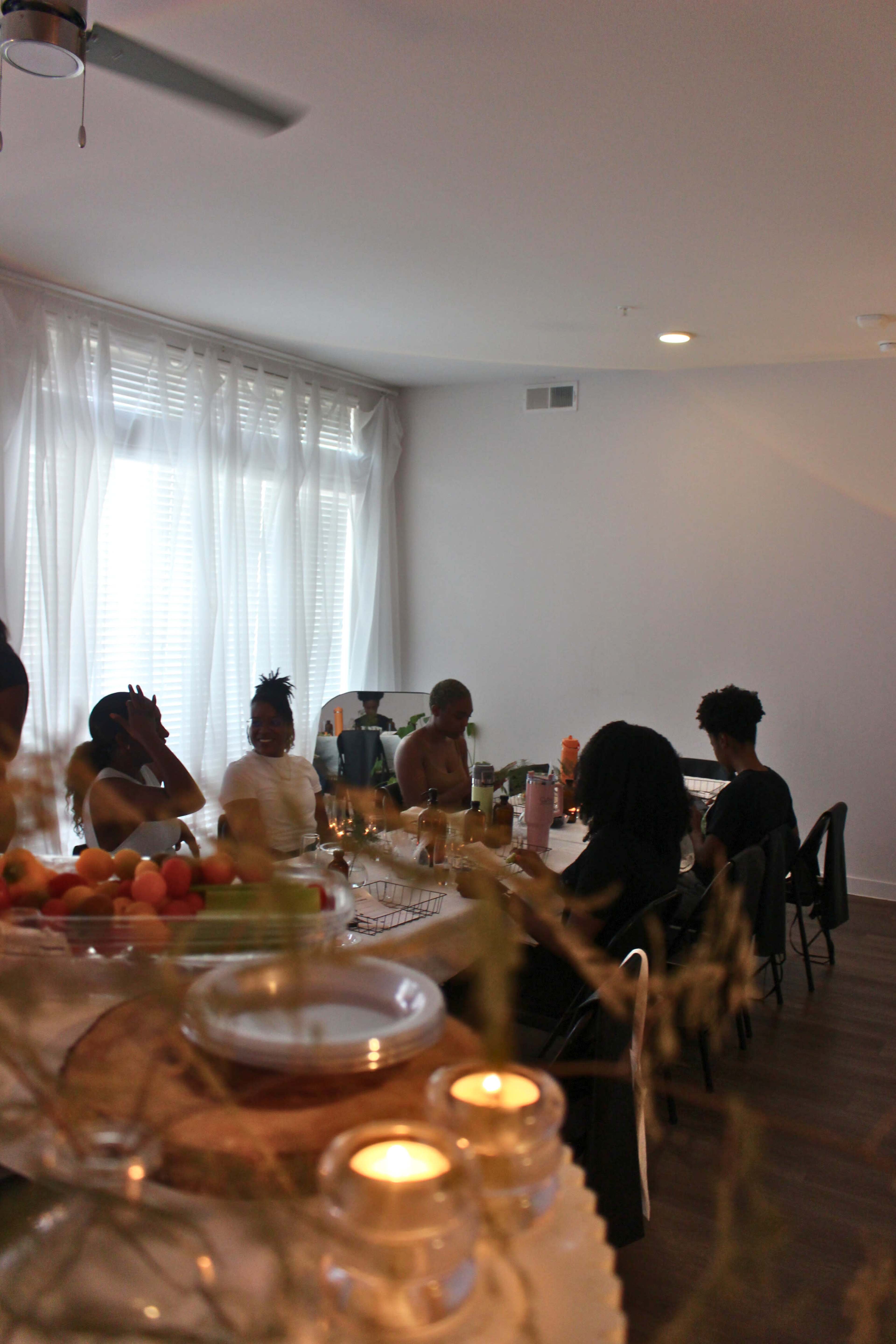 A group of people sit around a dining table, enjoying a meal in a bright, airy room with large windows.