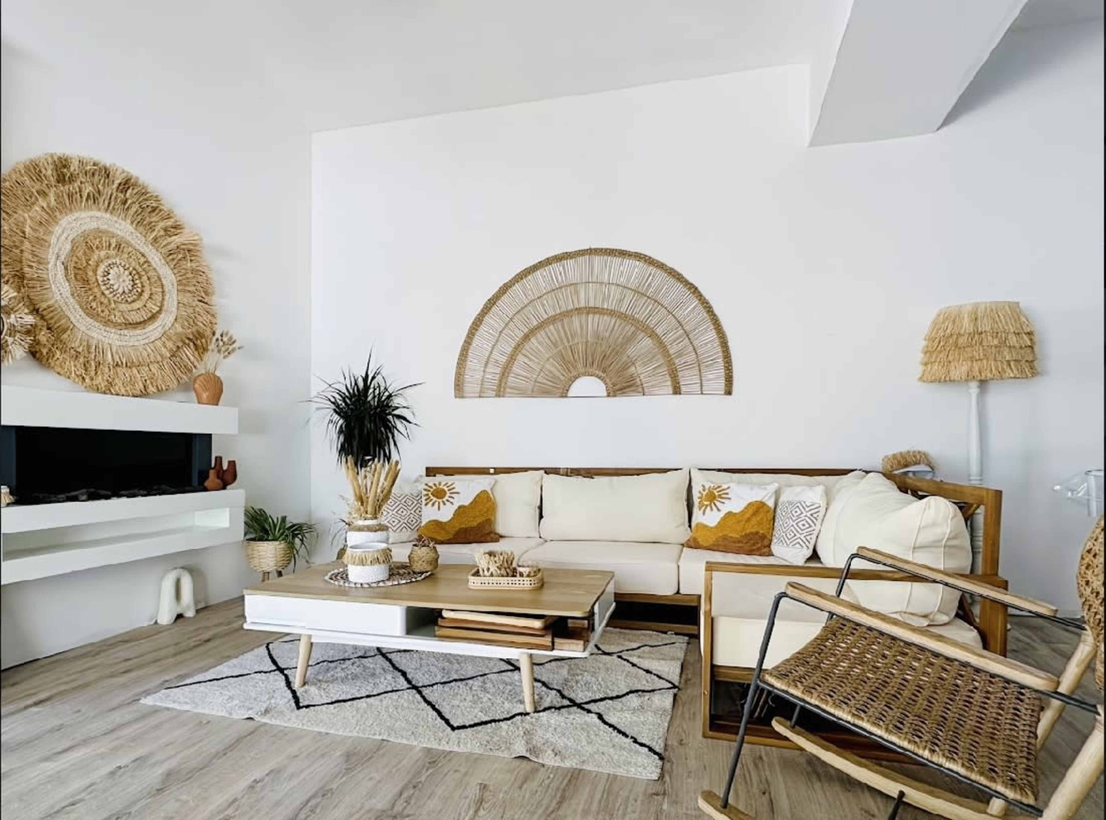 The image shows a modern living room featuring a wooden sofa with cream and mustard cushions, a coffee table, and decorative wall elements made of natural materials.
