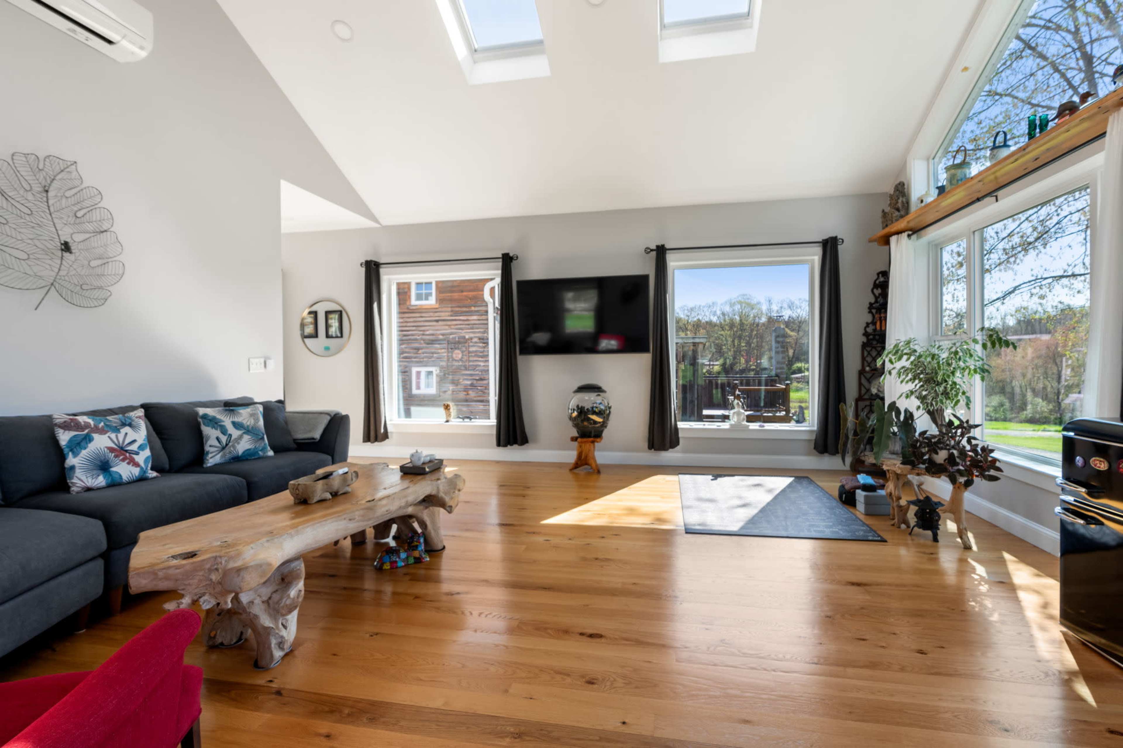 The room features a large wooden coffee table, a dark sofa with patterned cushions, and large windows that illuminate the space with natural light.