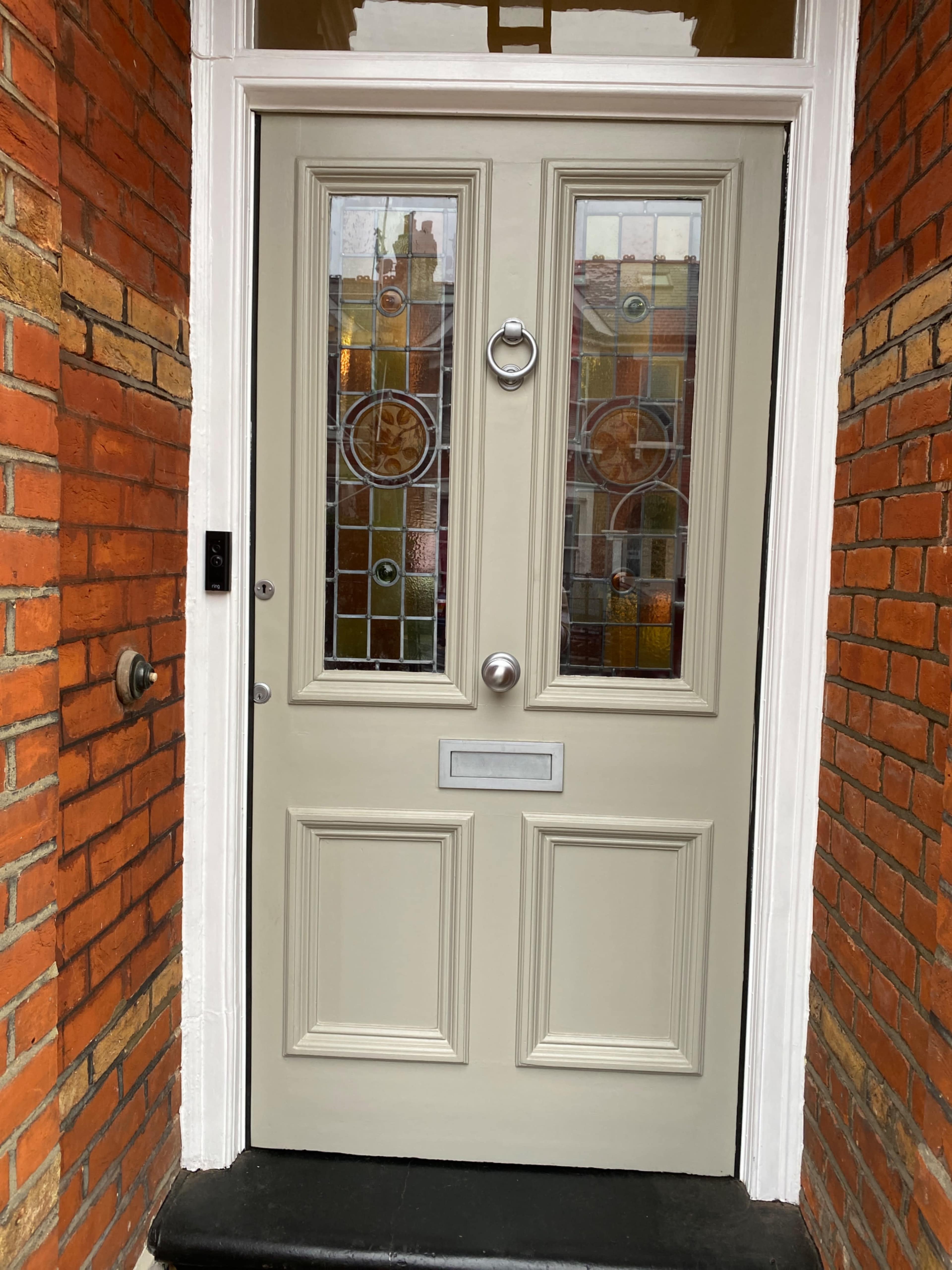 The image shows a wooden door with two rectangular panes of stained glass, framed by a brick wall on either side.