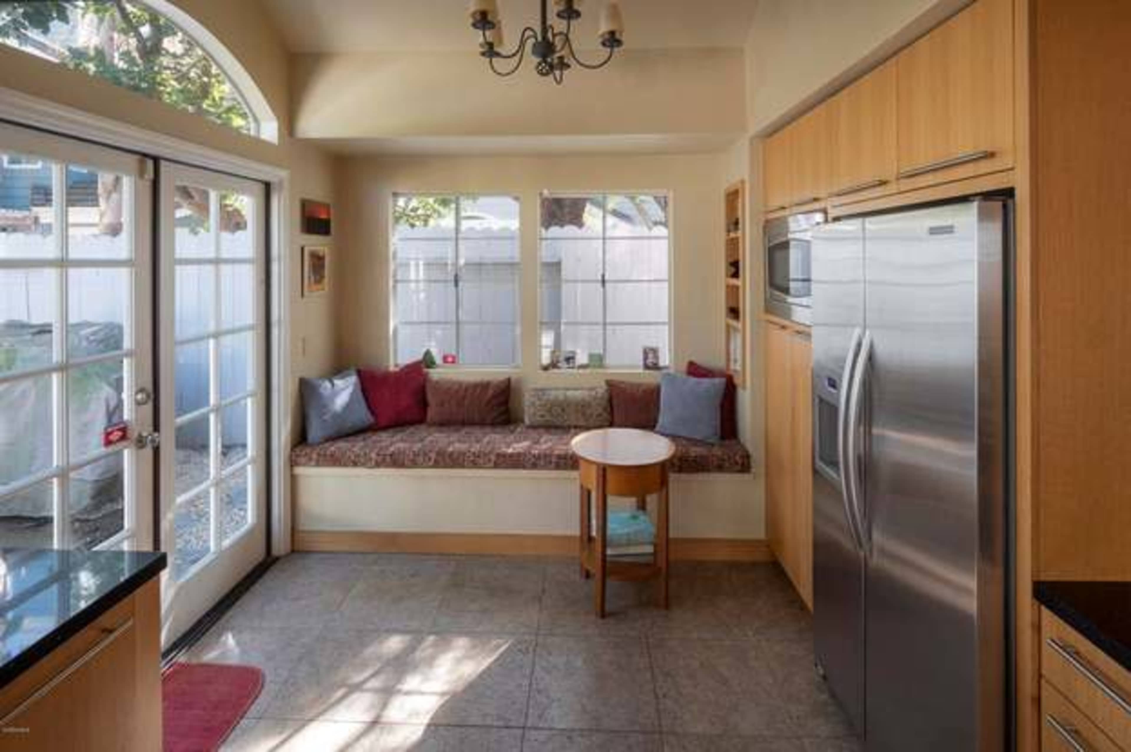A kitchen features a window seat with cushions and a small table, alongside stainless steel appliances and wooden cabinetry.