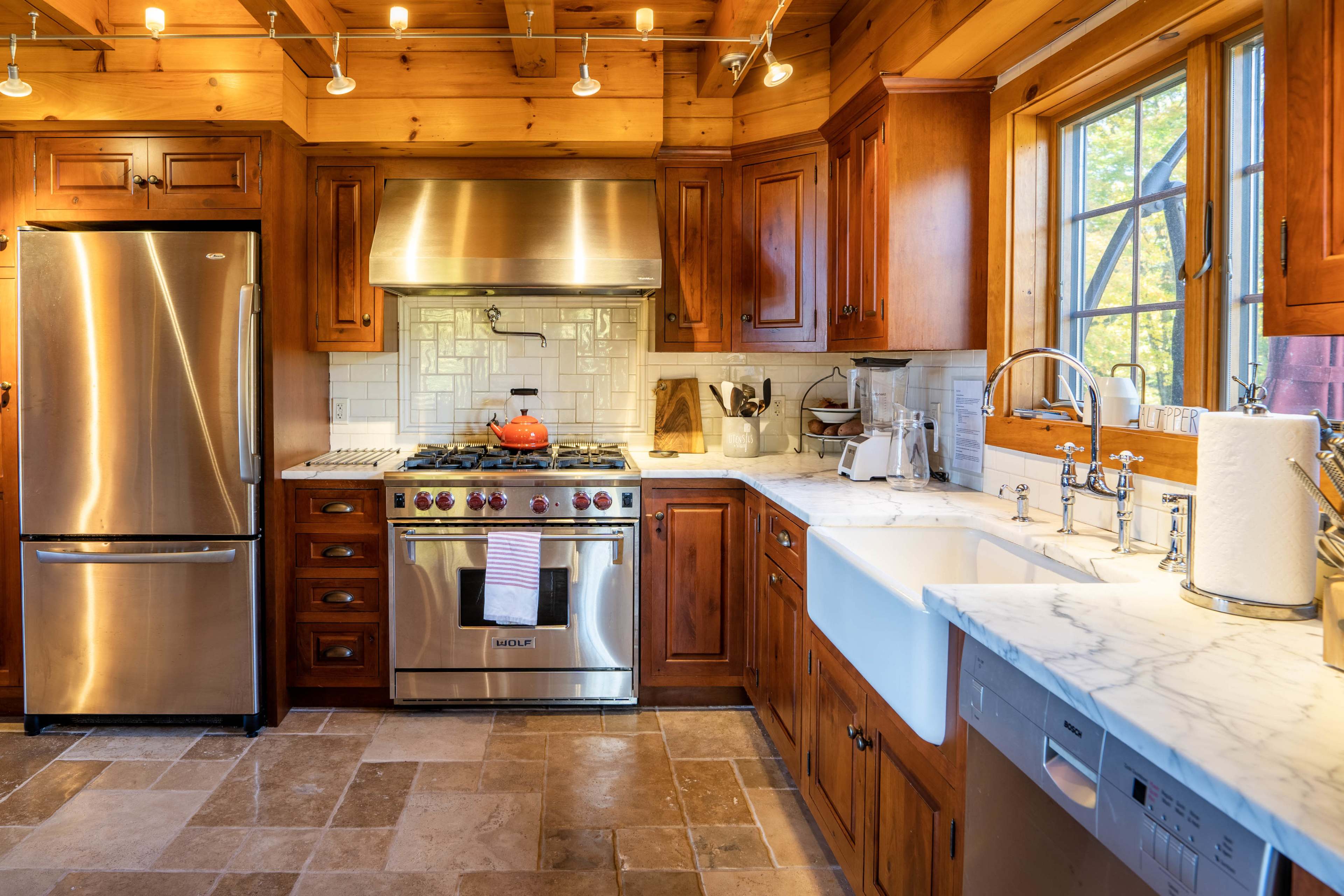 A modern kitchen features wooden cabinetry, stainless steel appliances, and a large farmhouse sink with marble countertops.