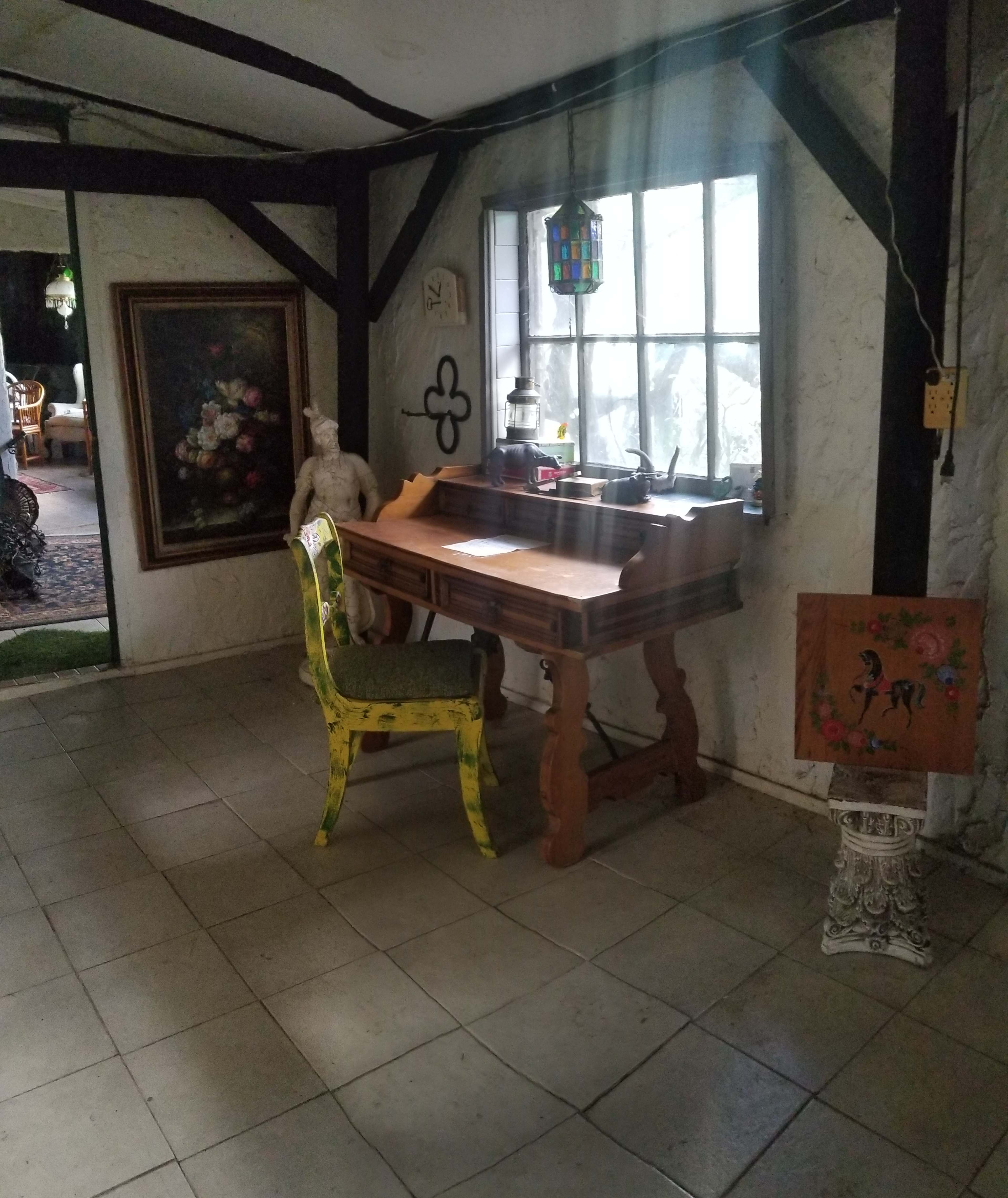 A wooden desk with a yellow chair beside a window in a room featuring rustic decor and artwork on the walls.