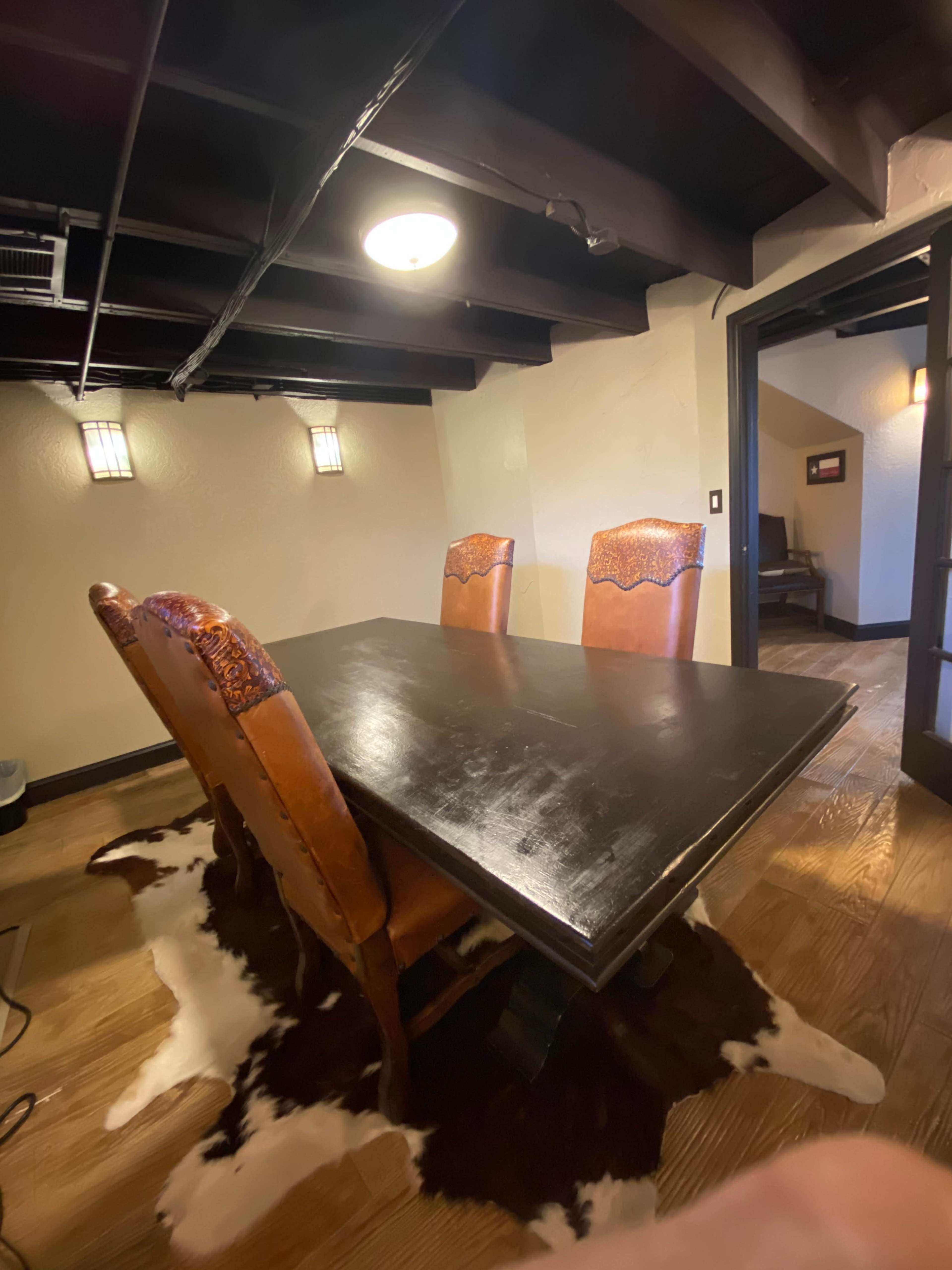 A room with a dark wooden dining table surrounded by four leather chairs, with a cowhide rug on the floor.