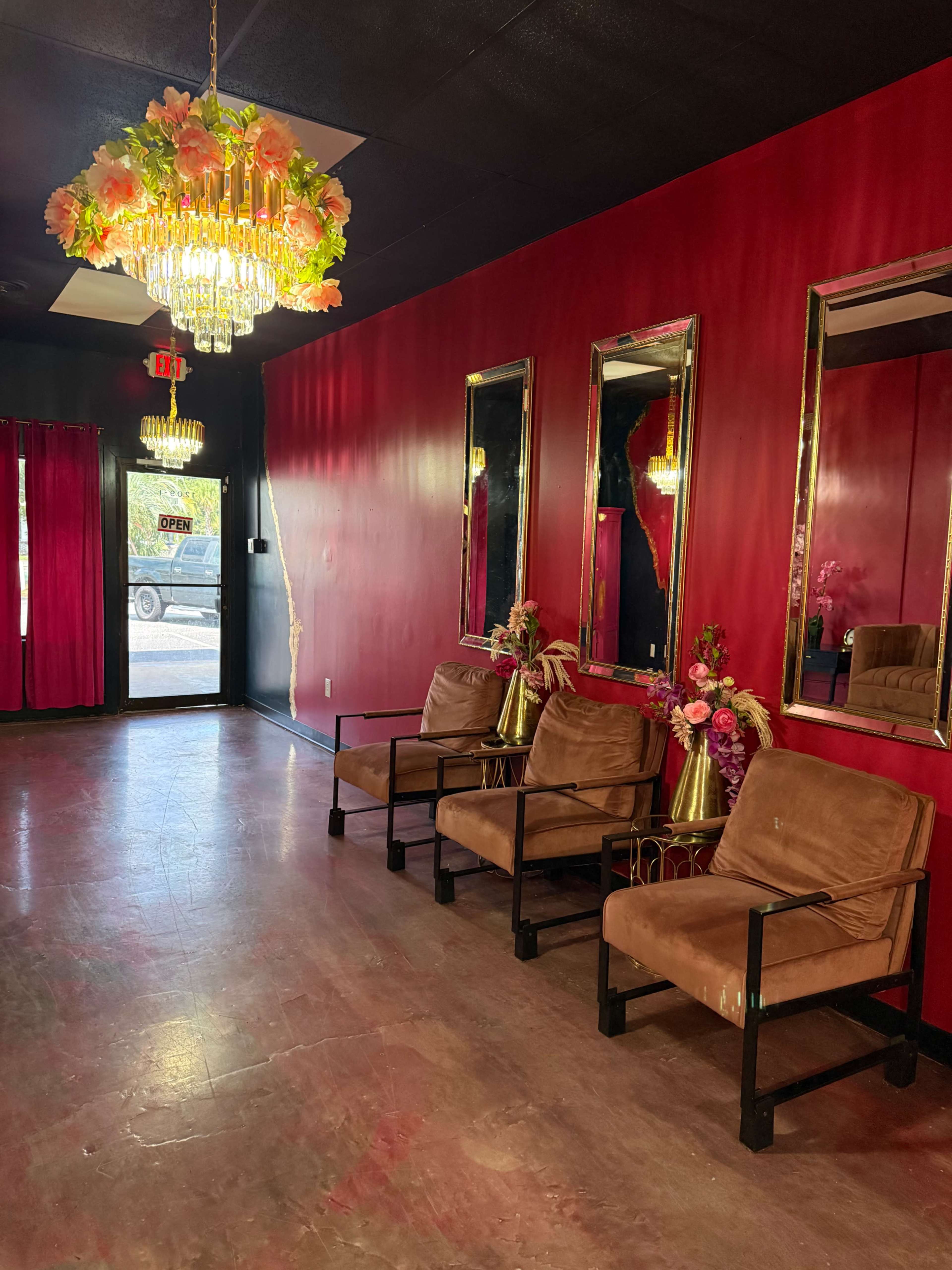 The image shows a waiting area with brown armchairs, a floral chandelier, and decorated mirrors against a red wall.