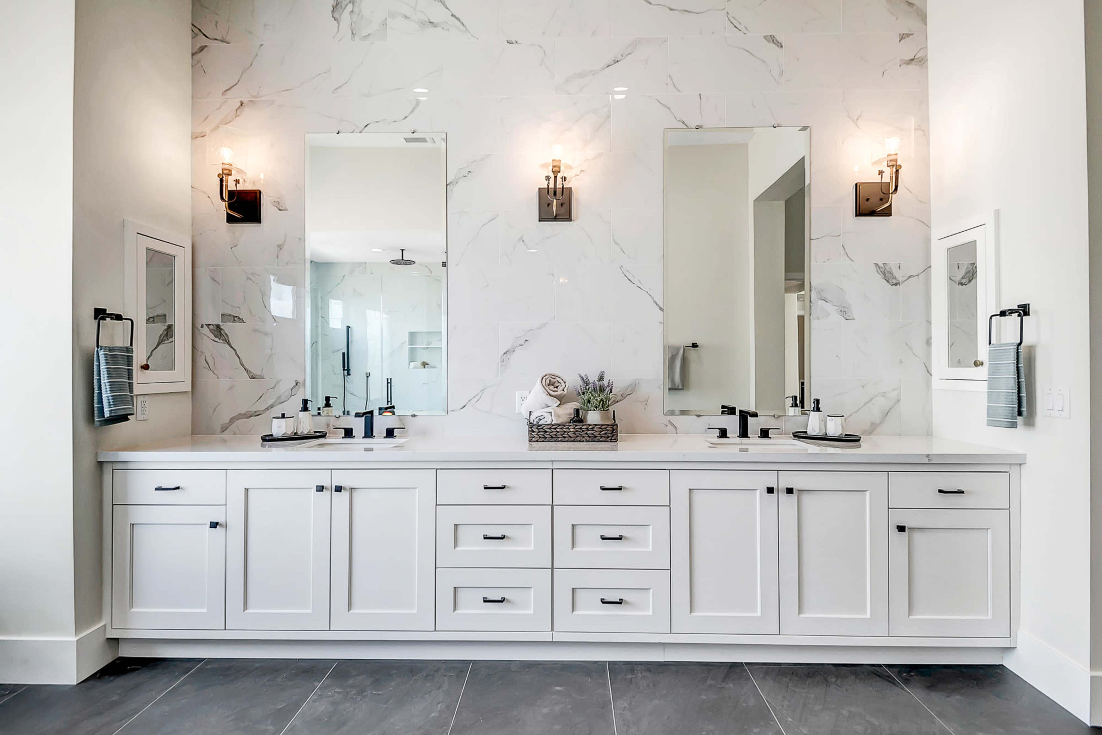 A modern bathroom with a dual vanity, two mirrors, and marble wall tiles.