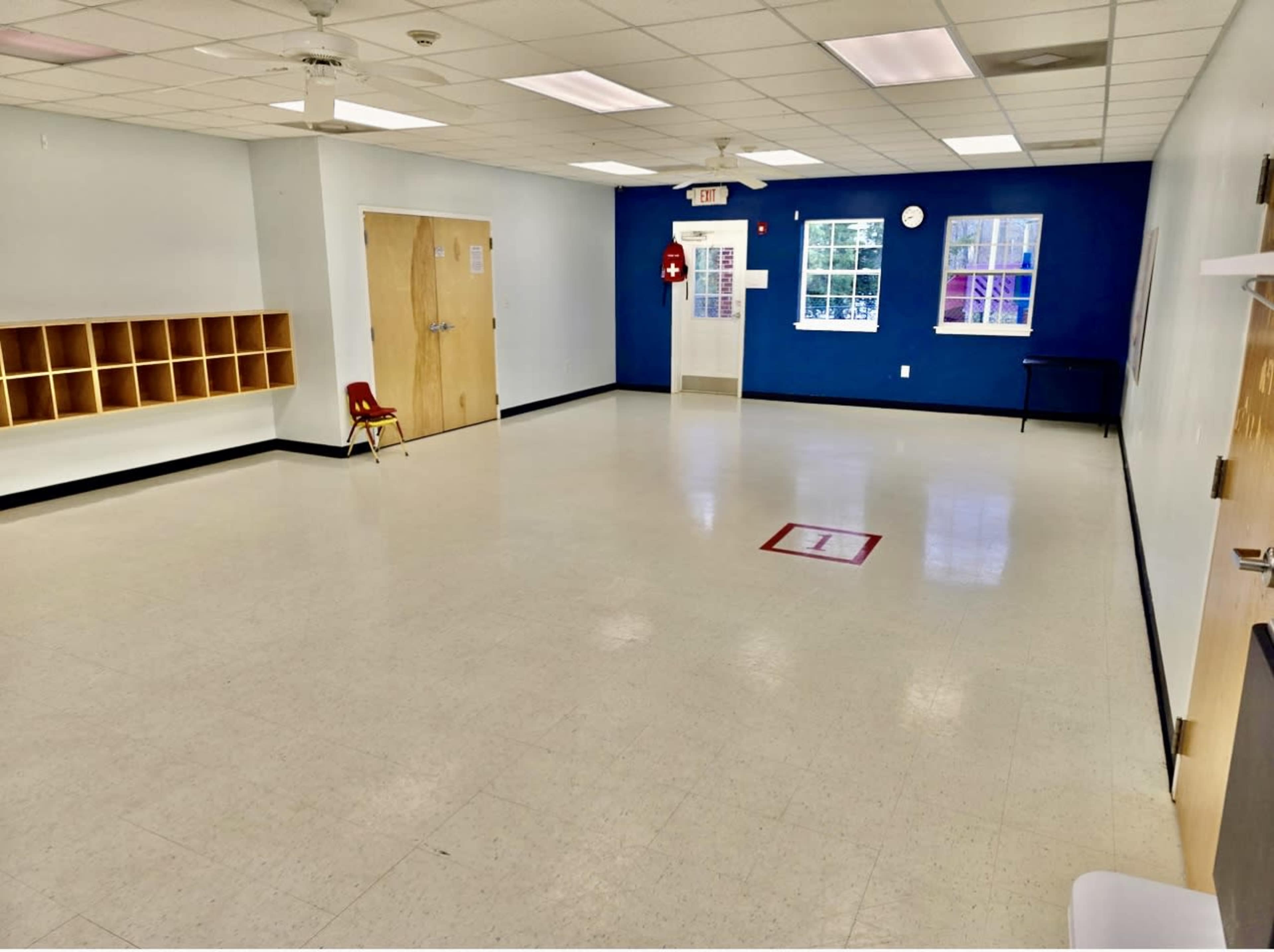 The room features a blue accent wall, a row of cubbies on one side, and minimal furniture, creating an open and spacious layout.