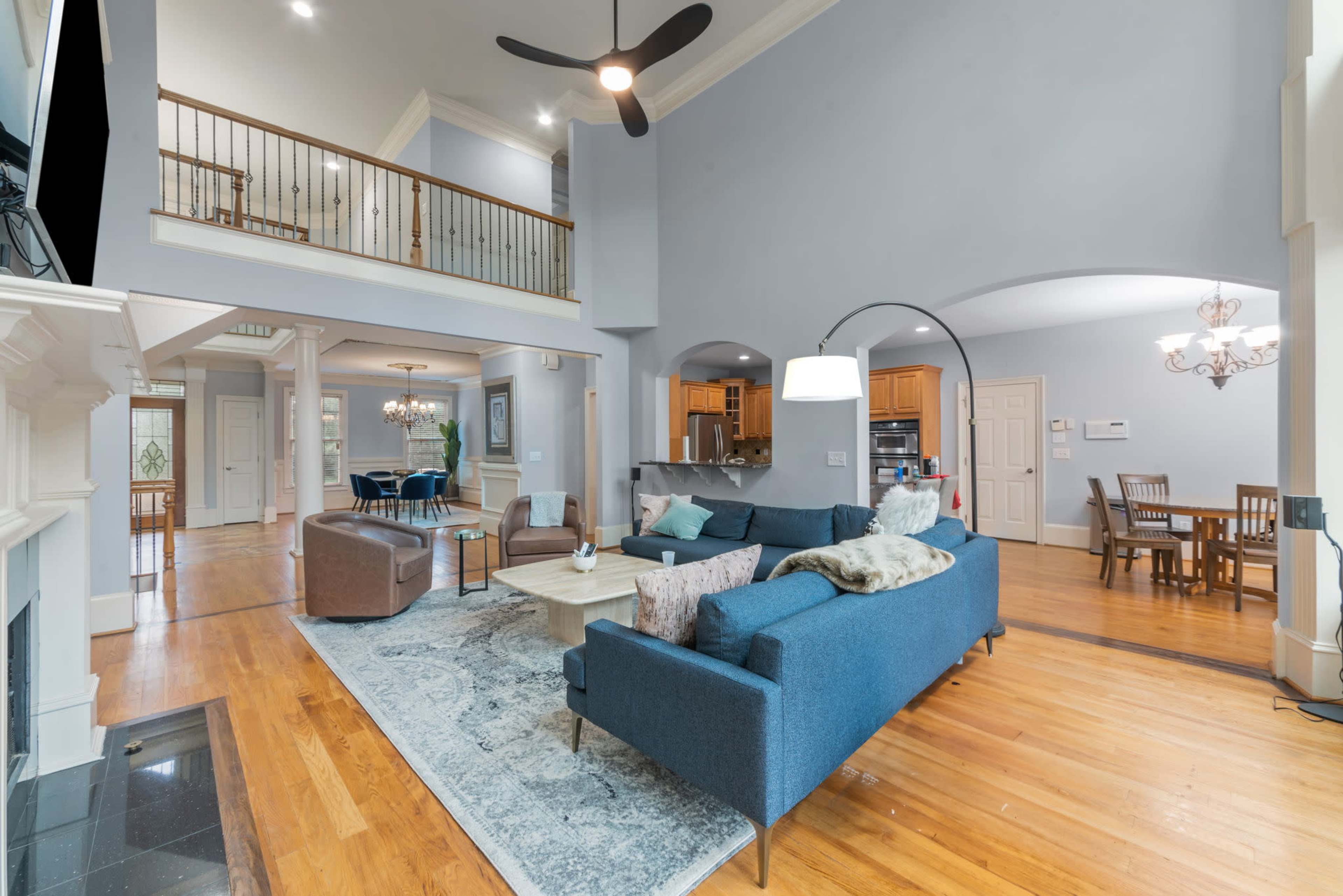 A spacious living room with a blue sofa, a coffee table, and a view of an open dining area and kitchen in a well-lit home.