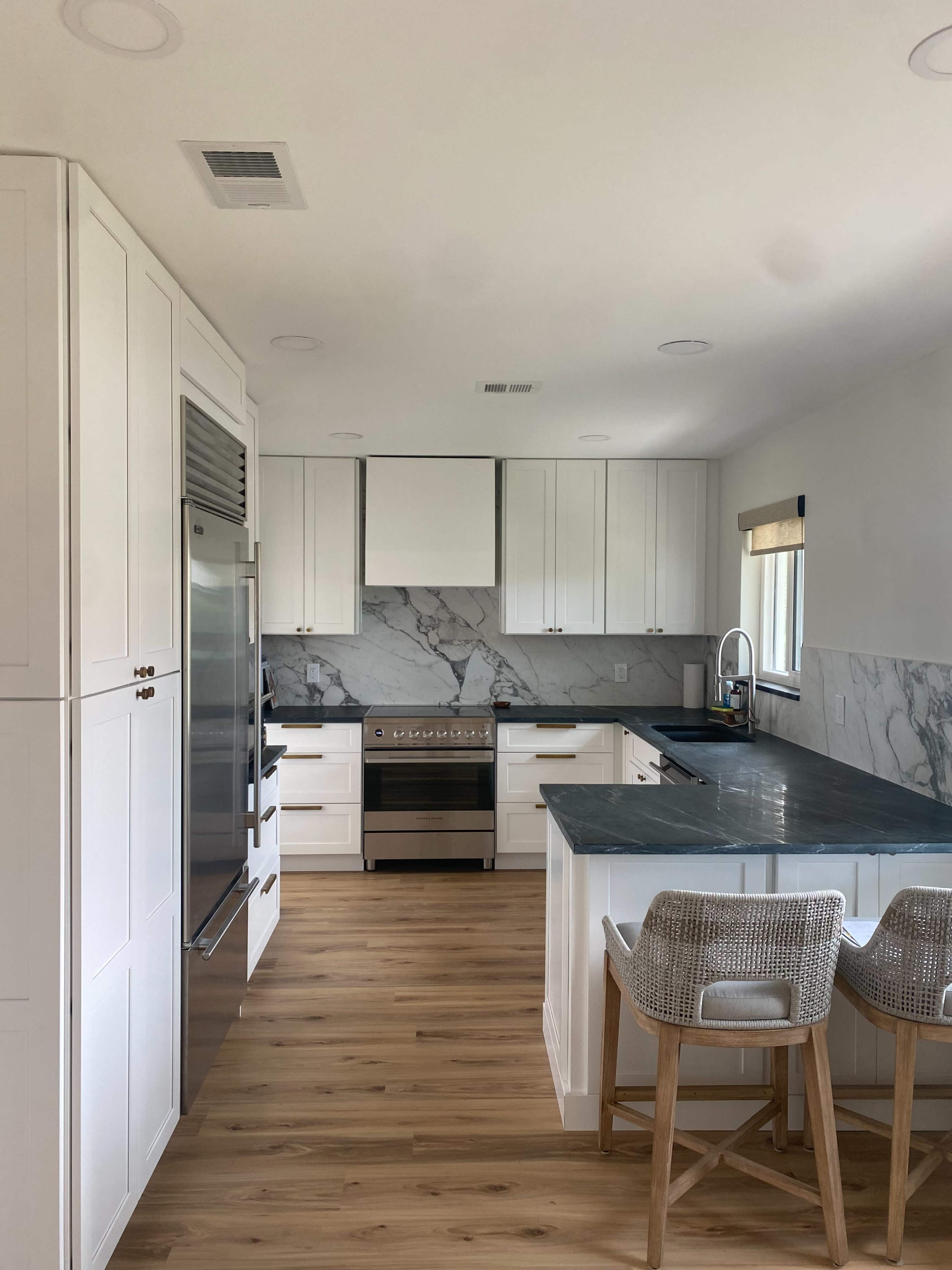 A modern kitchen features white cabinets, a marble backsplash, stainless steel appliances, and a wooden floor.