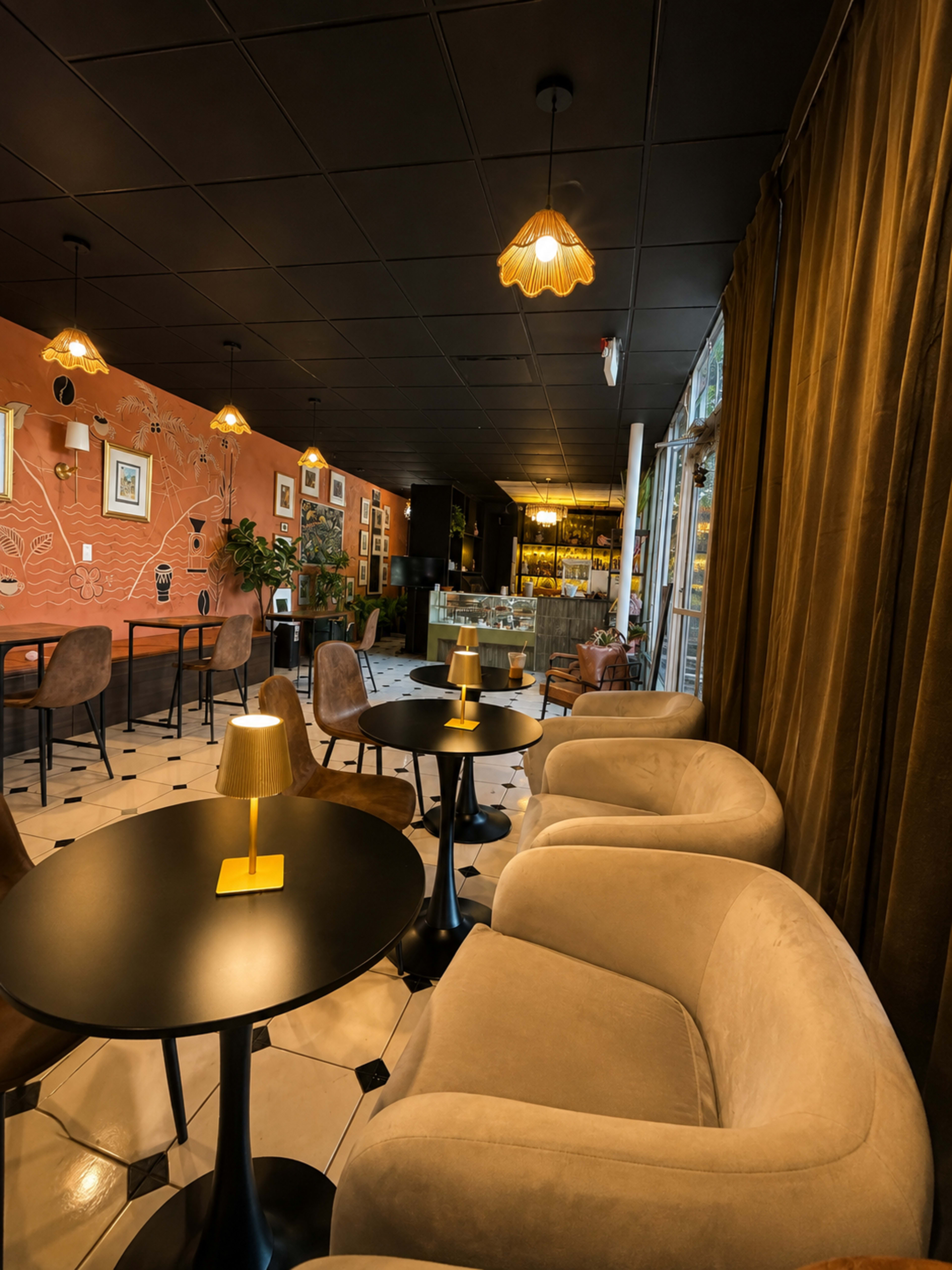 The image shows a cozy café interior featuring plush chairs and small tables, with warm lighting and a decorative wall.