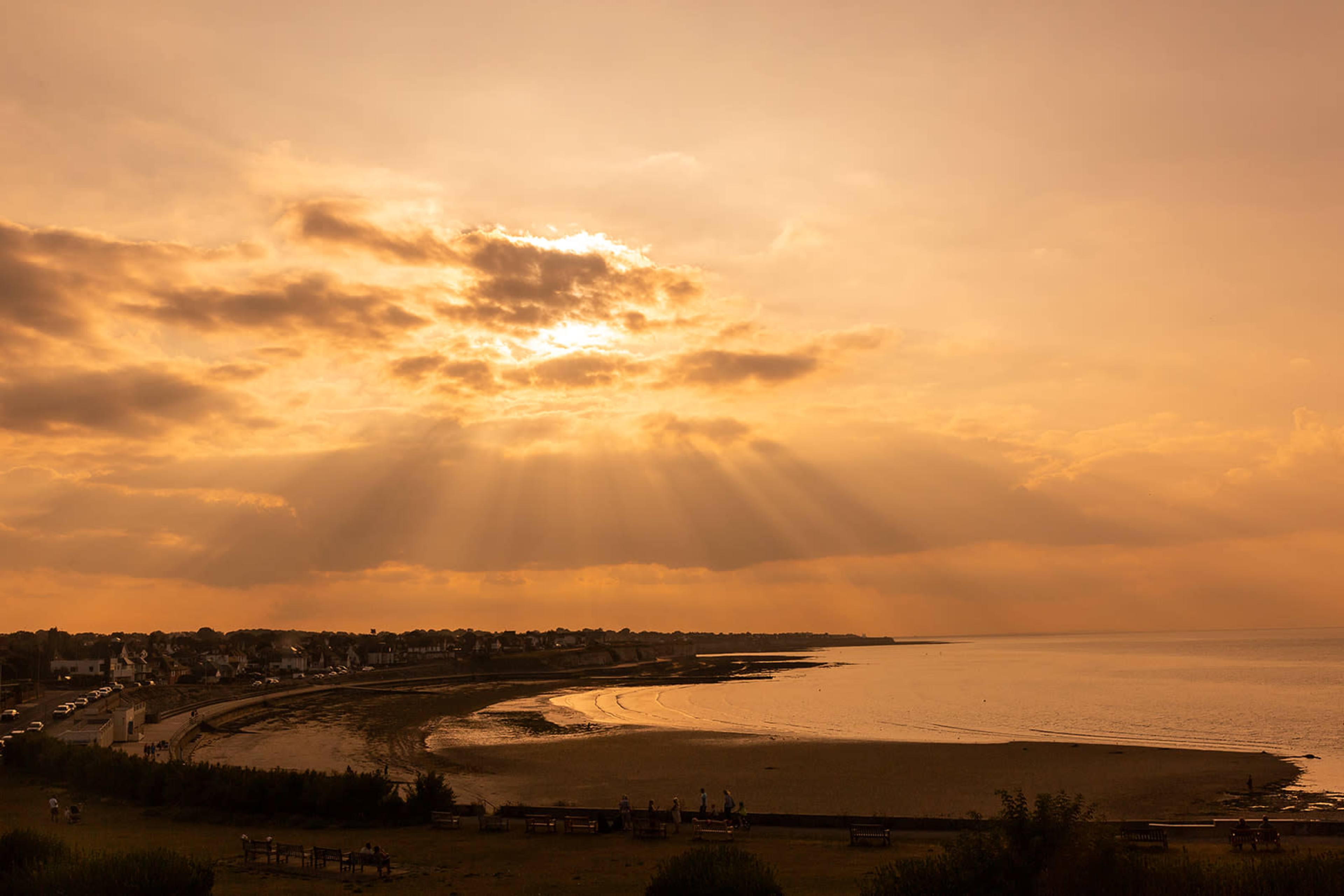The image shows a beach at sunset with rays of sunlight breaking through the clouds over the water.