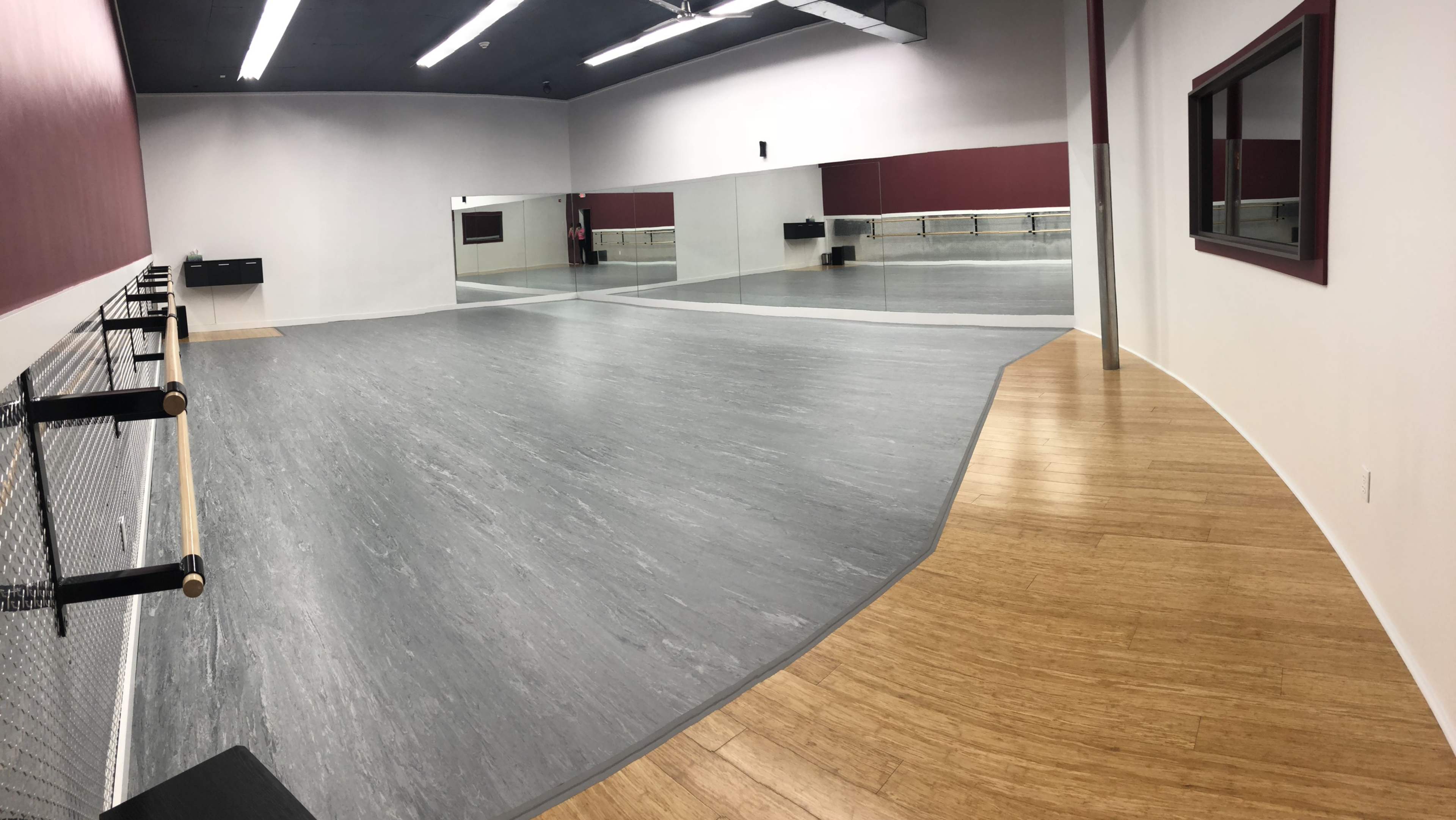 A spacious dance studio with mirrored walls, wooden flooring, and ballet bars along one side.
