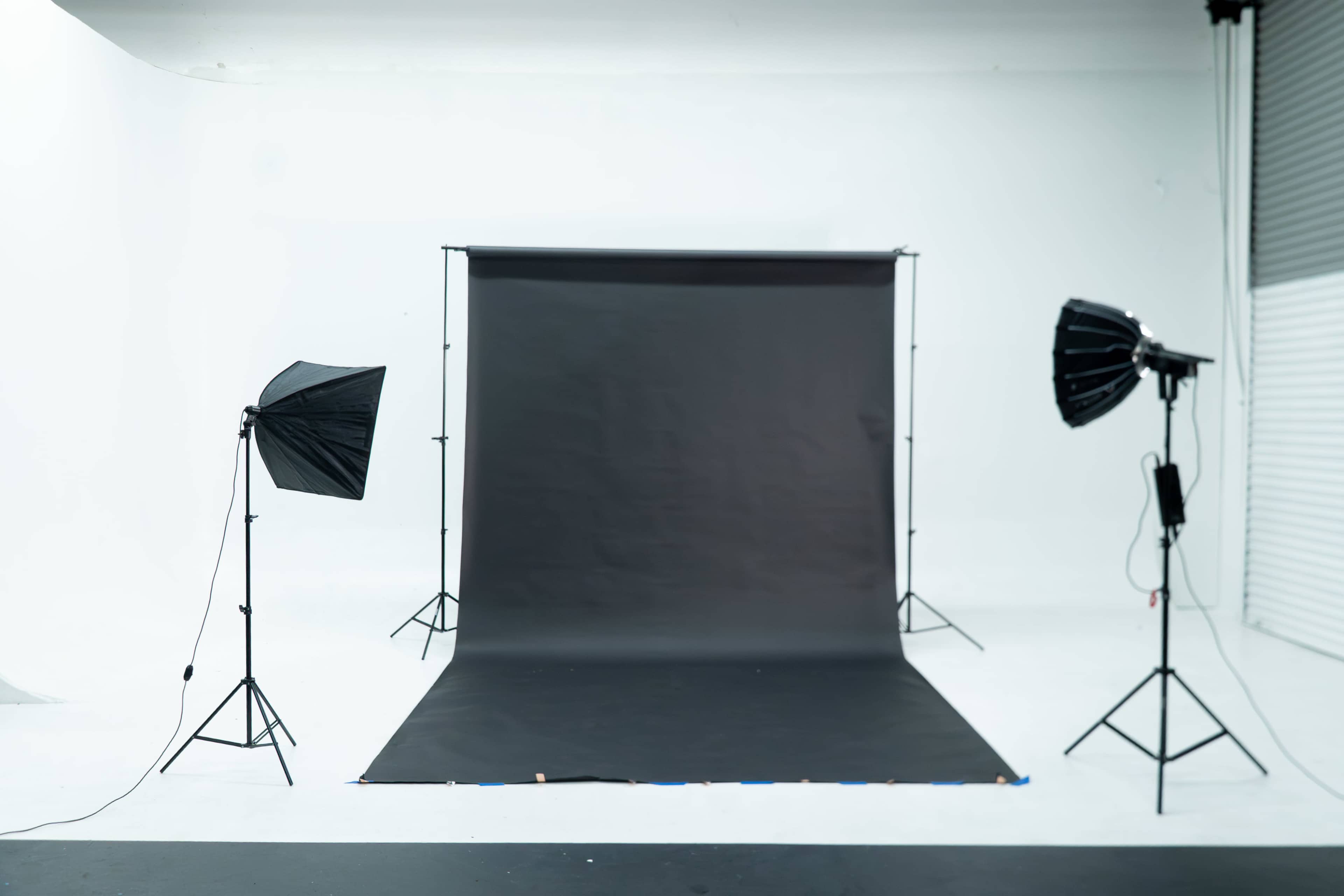 A photography studio features a black backdrop set up between two light stands with softboxes on either side.