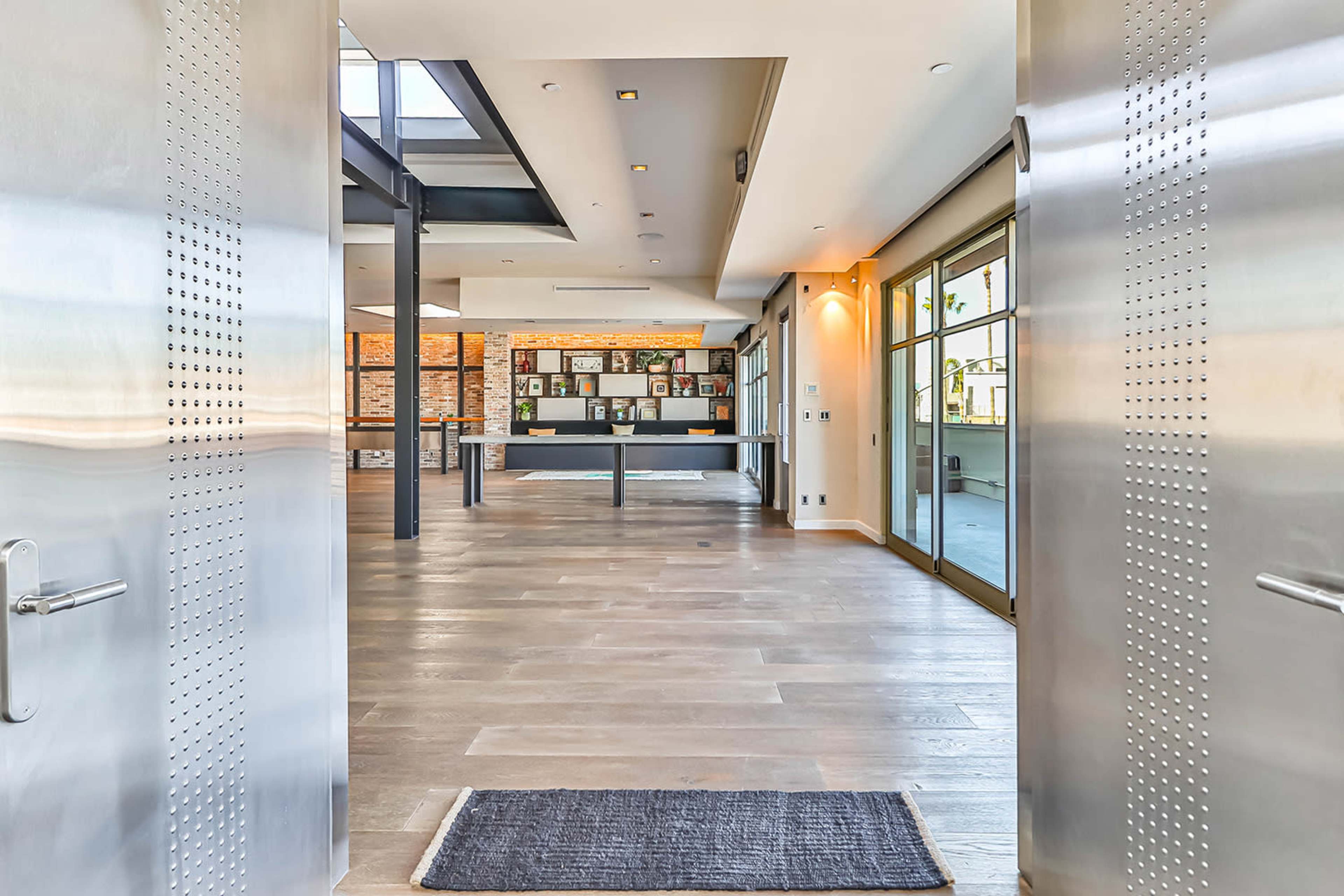 A modern entryway with large stainless steel doors leading into a bright, open interior space featuring wooden flooring and a gallery area with framed photos.