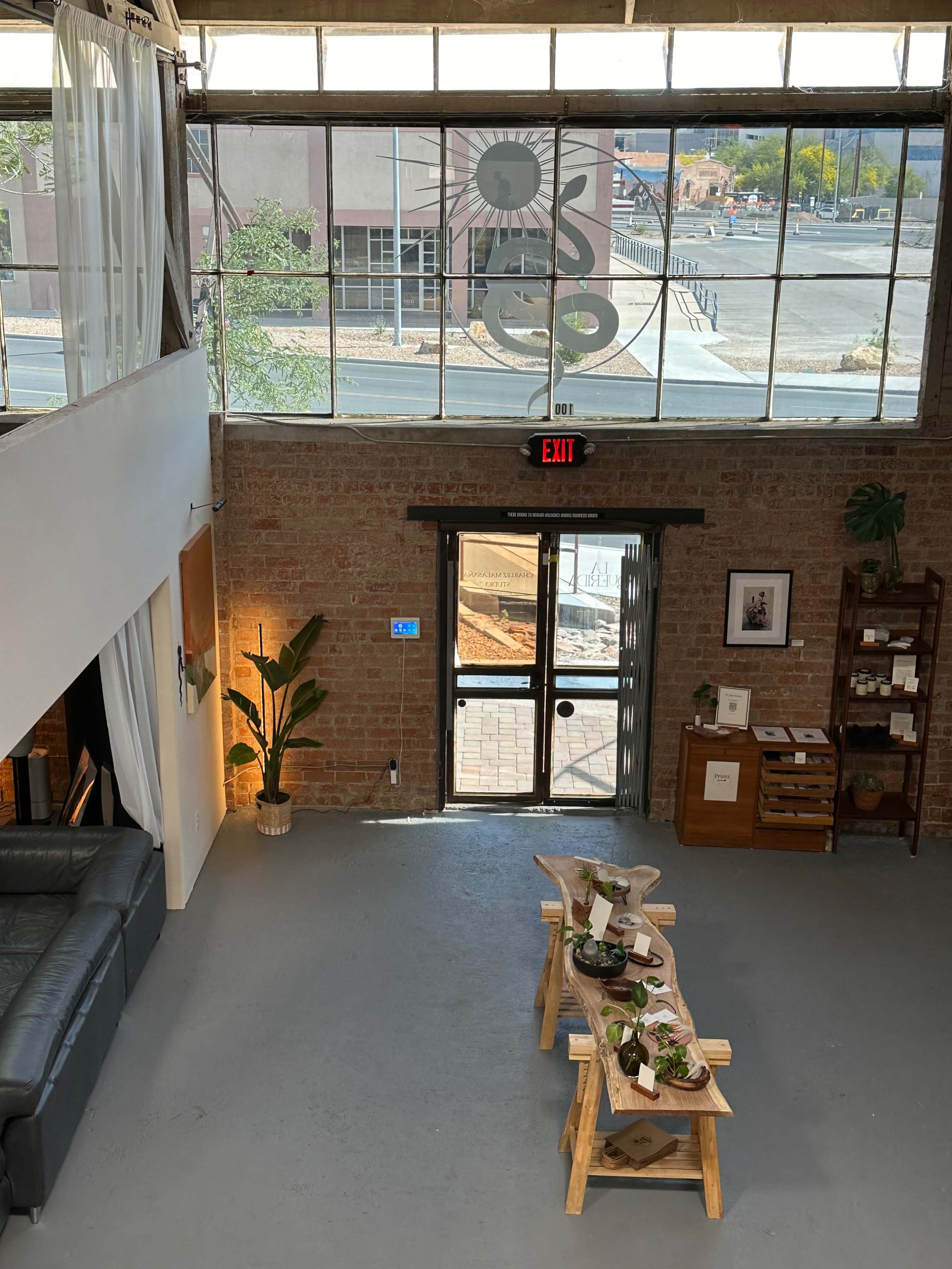 A modern interior of a space with large windows, a seating area, and a table displaying plants, leading to an exit door.