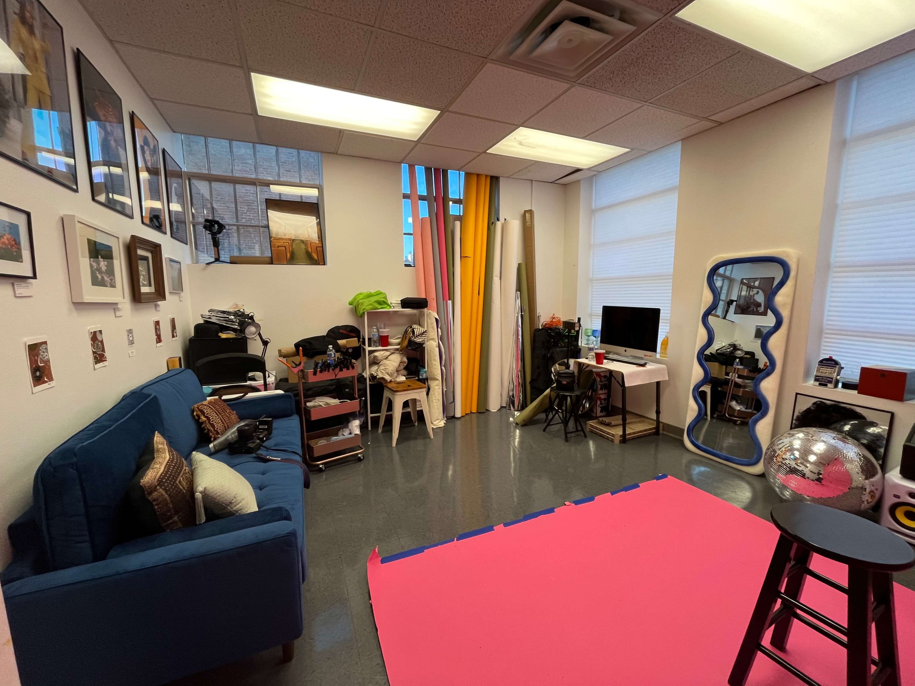 A small room with a blue couch, a pink floor mat, various props and equipment, and a window with bright yellow curtains.