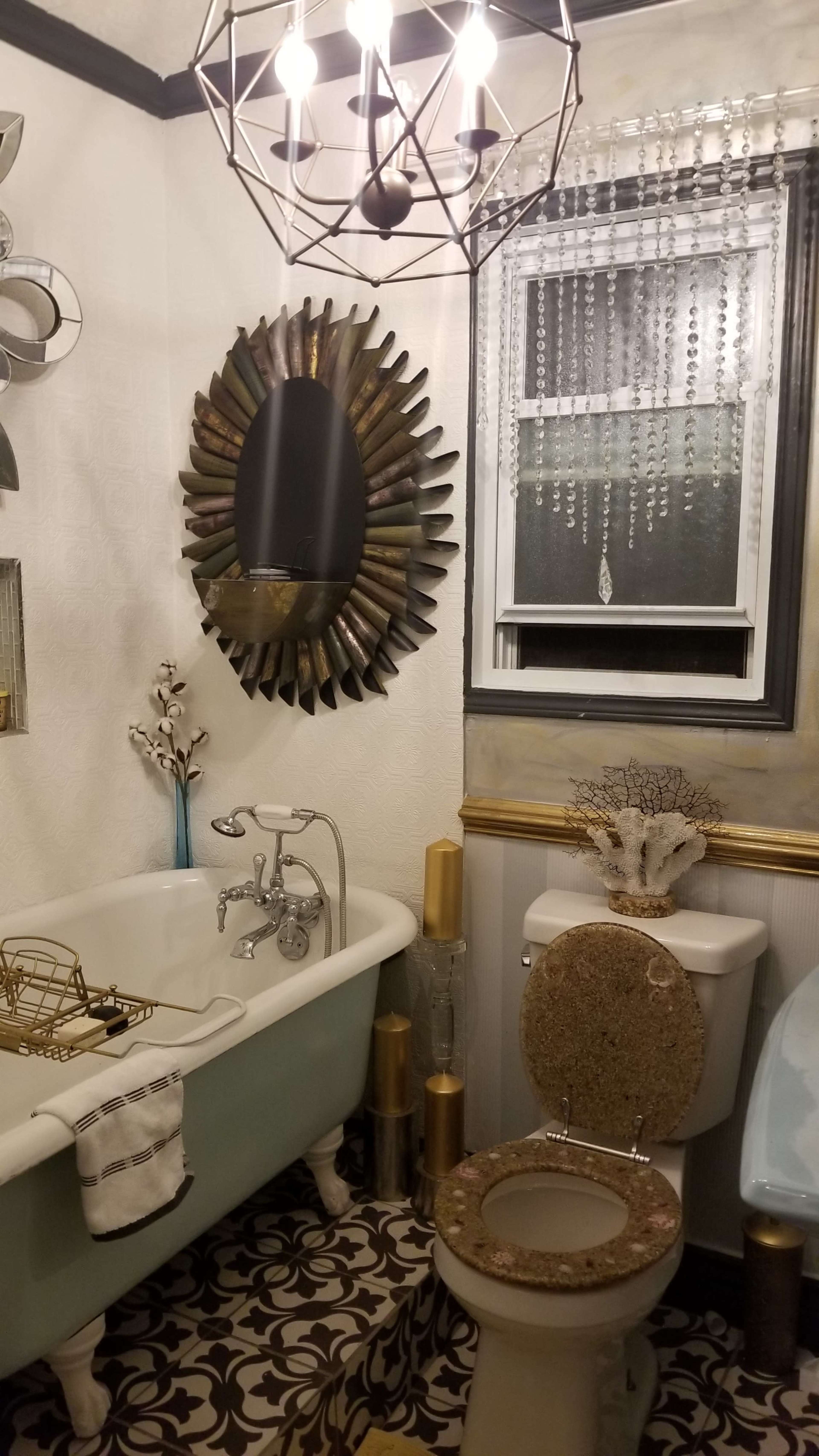 A bathroom featuring a freestanding bathtub, a decorative mirror, a chandelier, and patterned flooring.