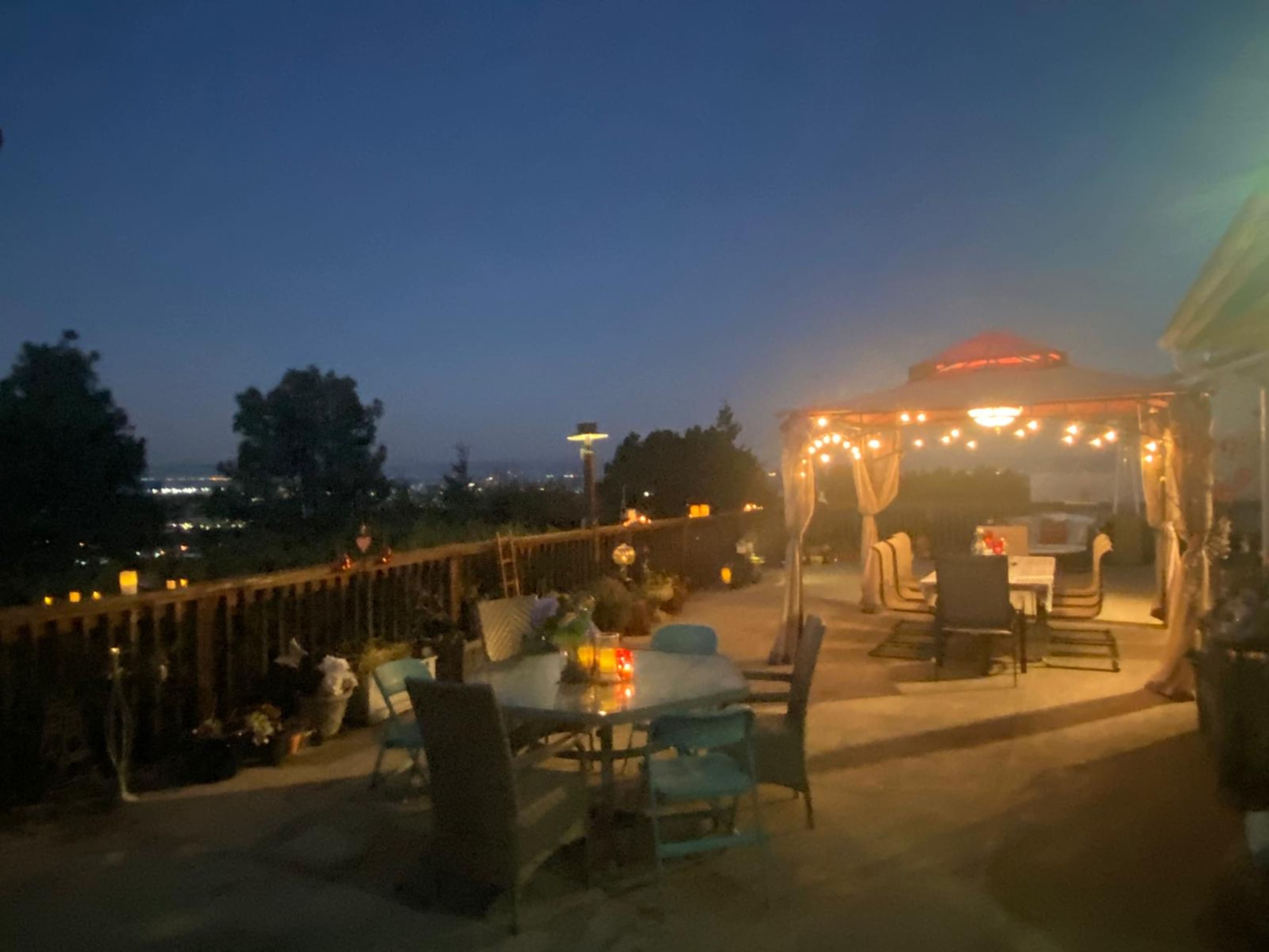 A patio area adorned with string lights and a gazebo, overlooking a nighttime landscape with distant city lights.