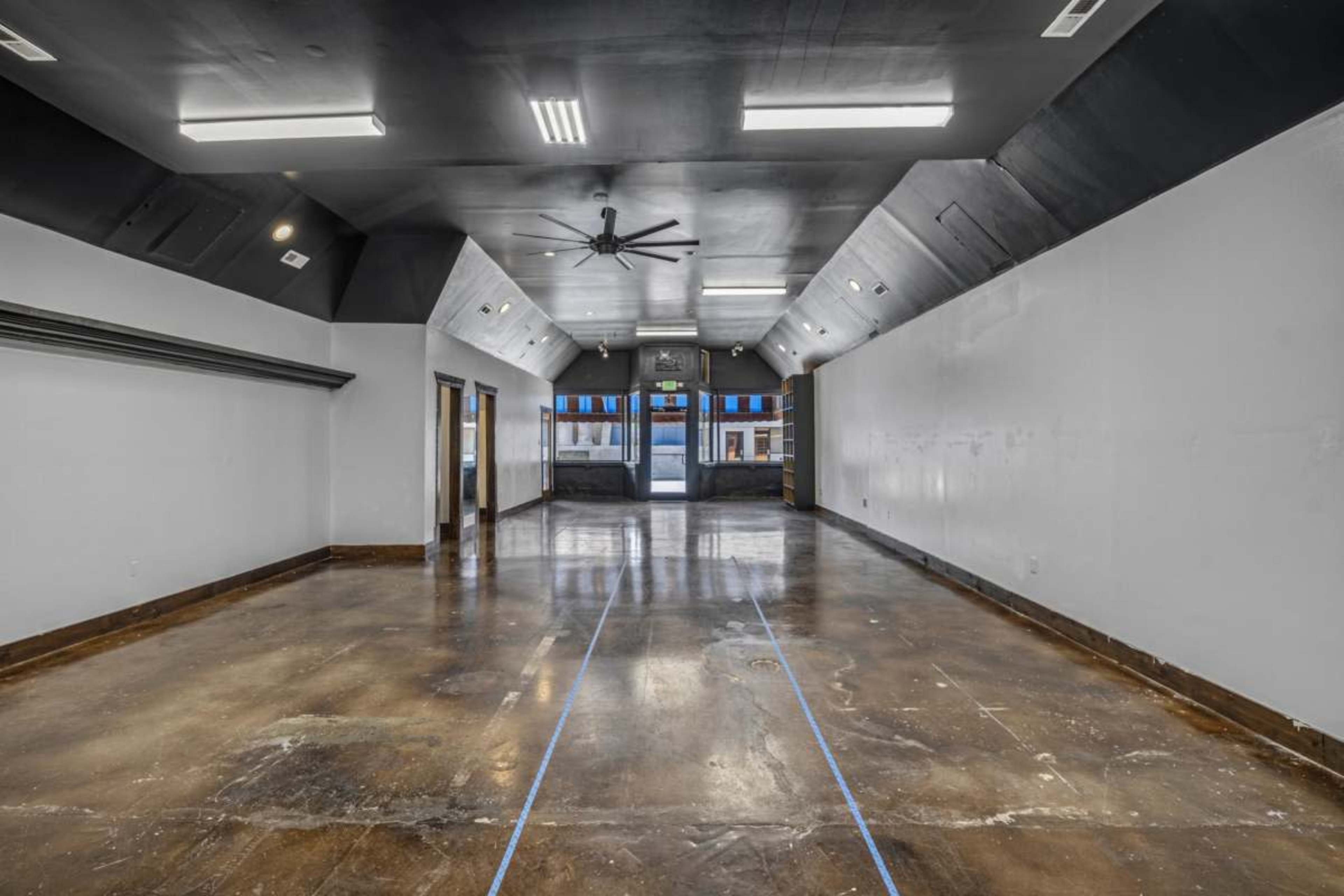 The image shows a spacious, empty room with polished concrete floors and large windows.