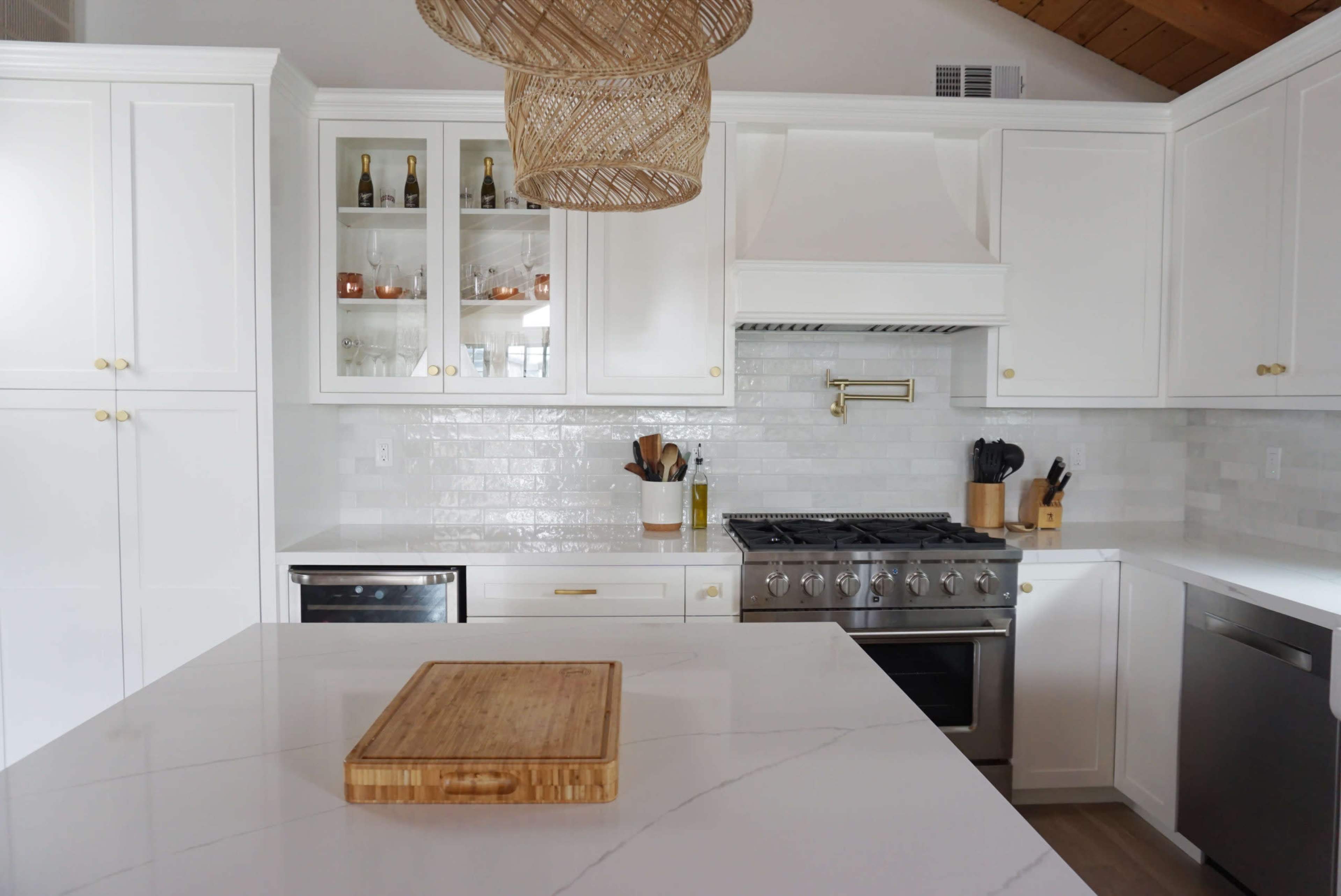 A modern kitchen features white cabinetry, a large marble island with a wooden cutting board, and stainless steel appliances.