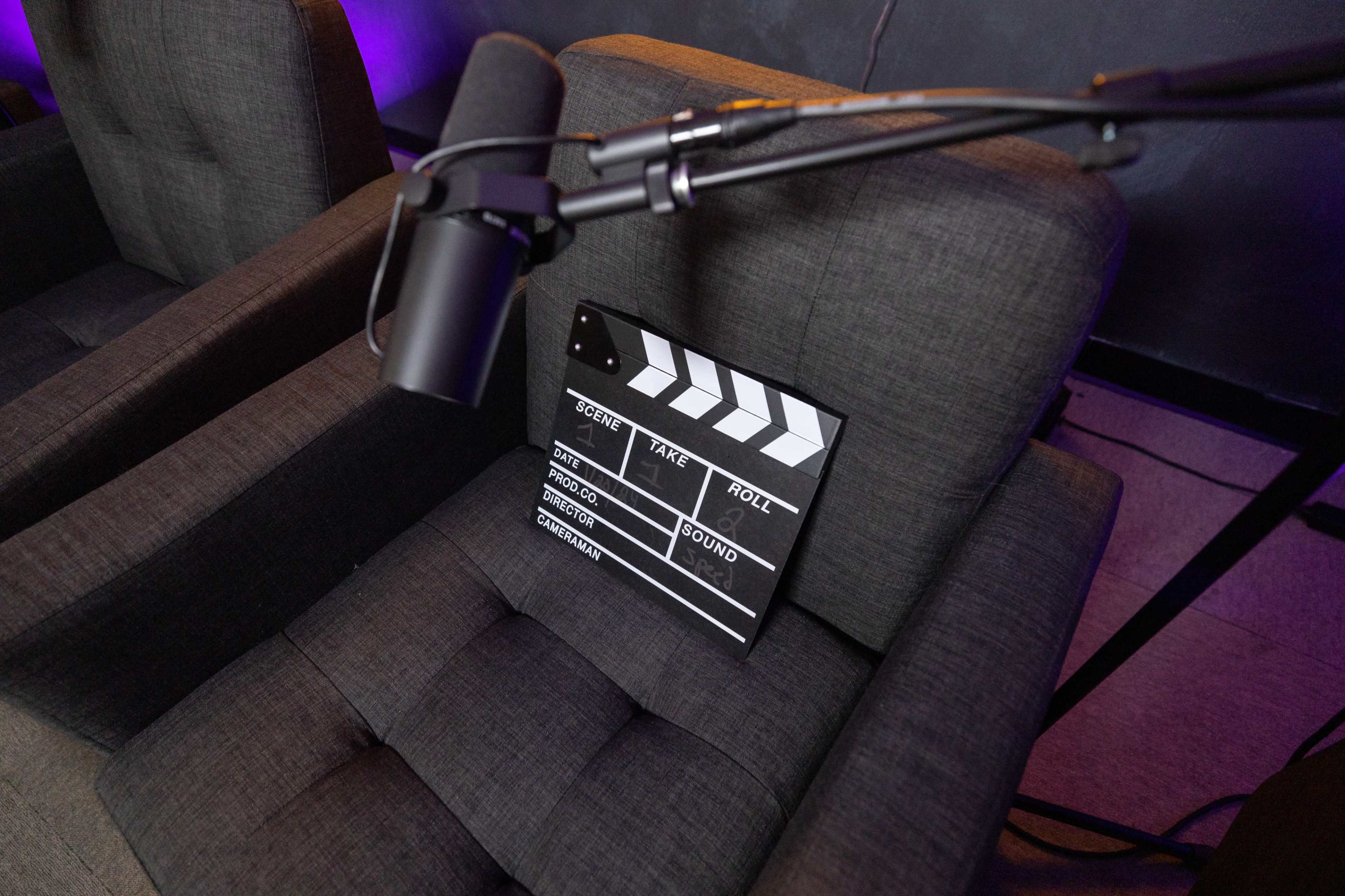 A film slate is placed on a gray armchair beside a microphone in a dimly lit recording studio.