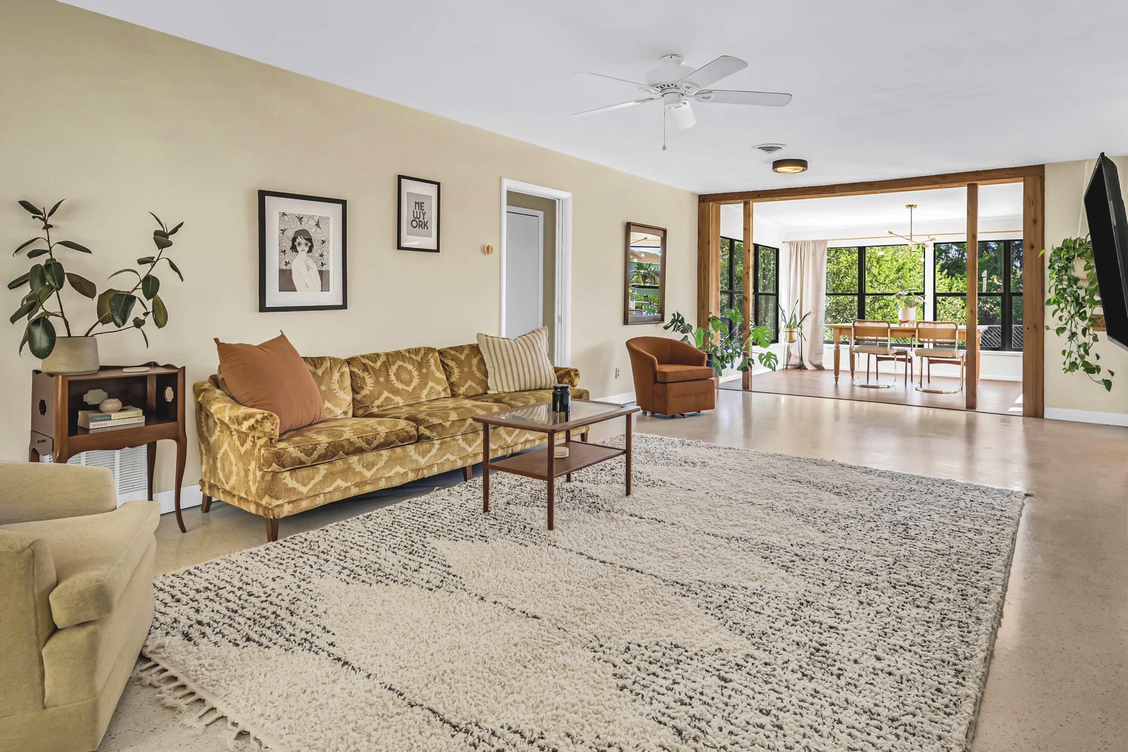A living room with a patterned rug, a brown couch, a coffee table, and a view into a dining area with large windows.