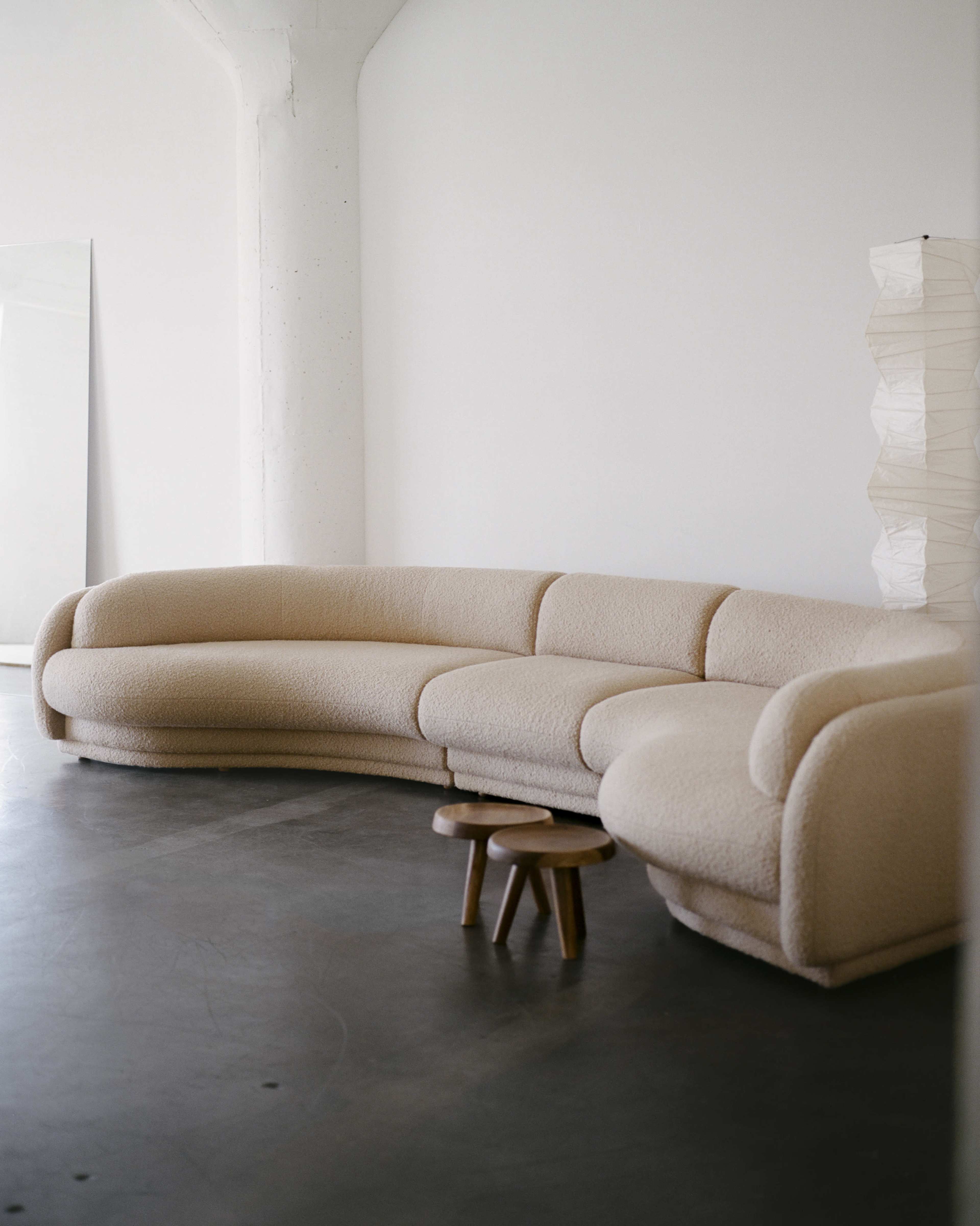 A curved, beige sofa is positioned in a minimalistic space with a small wooden table in front.