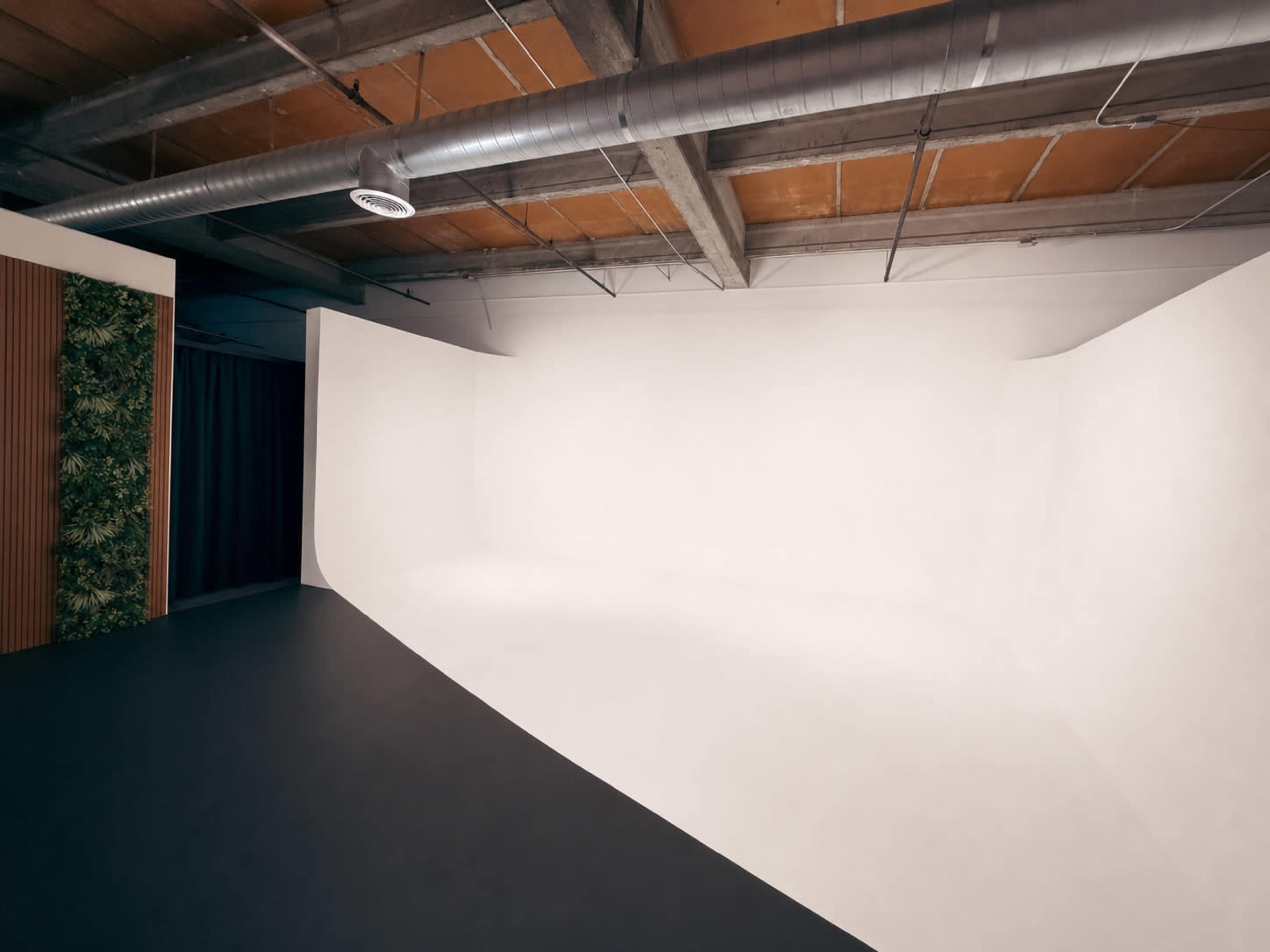 The image shows a spacious interior with a curved white backdrop, dark flooring, and visible metal ductwork on the ceiling.