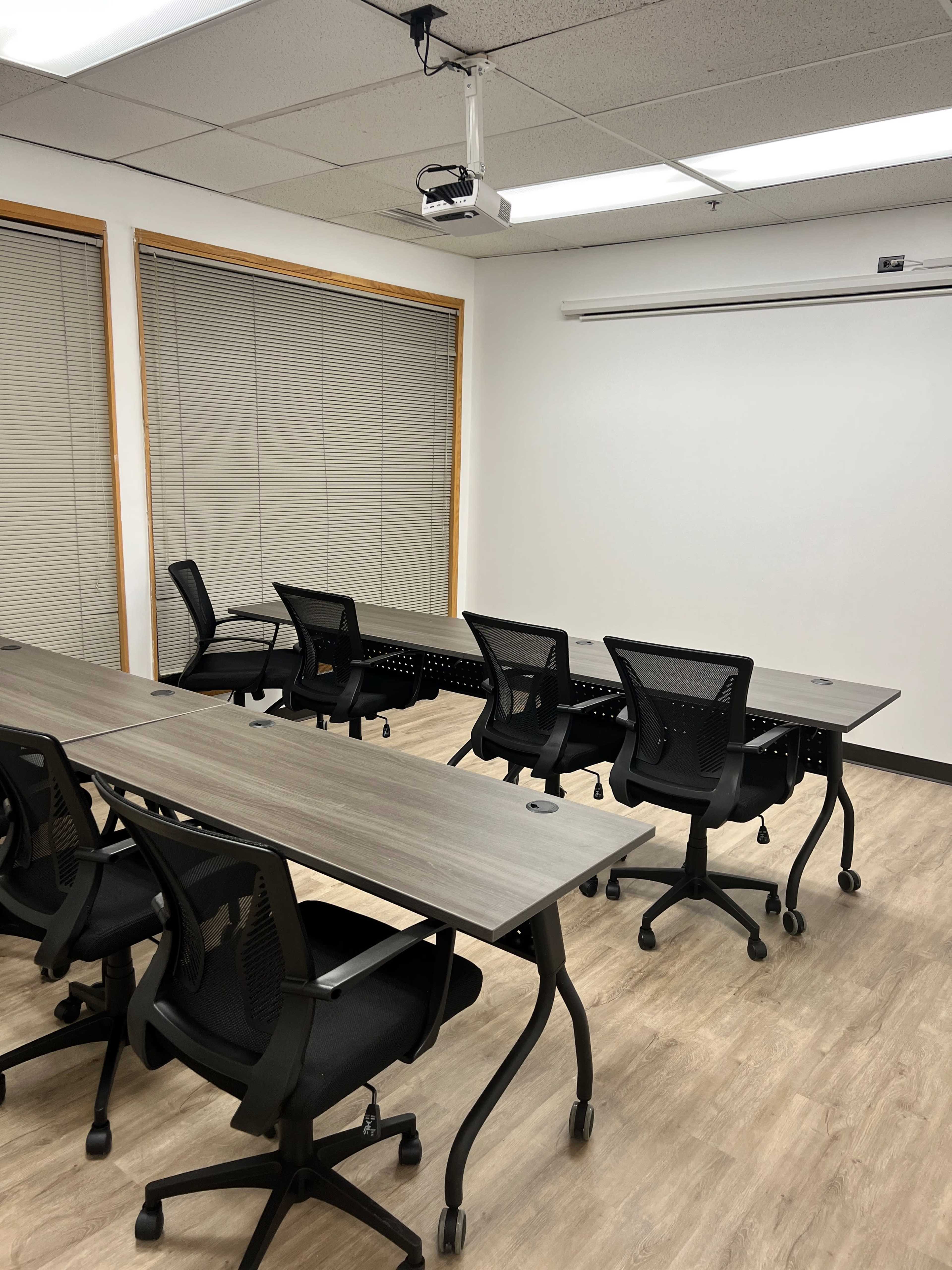 A modern conference room features several mobile desks and chairs arranged around a screen and projector.