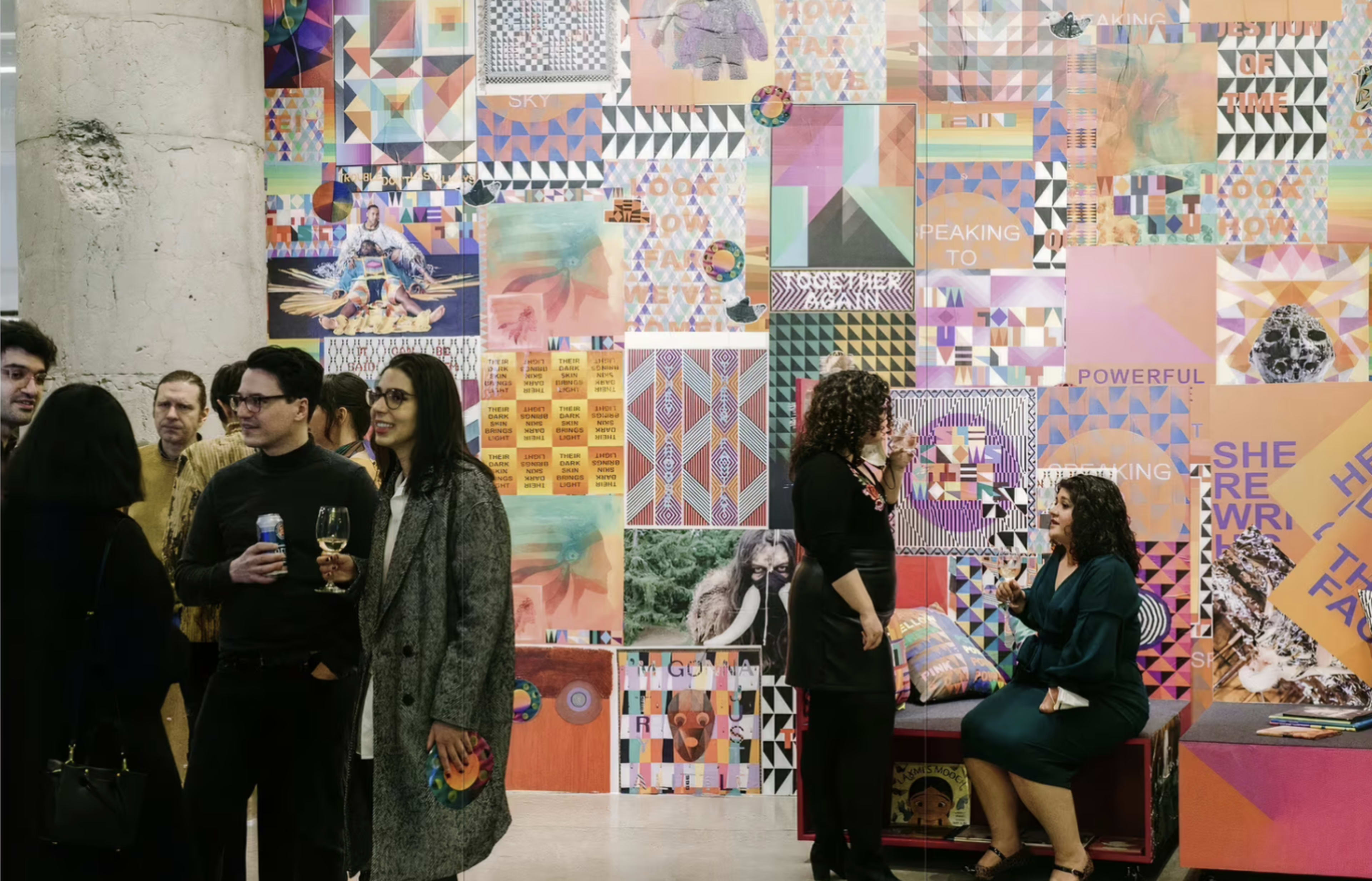 A group of people socialize in front of a colorful, abstract mural at an art event.