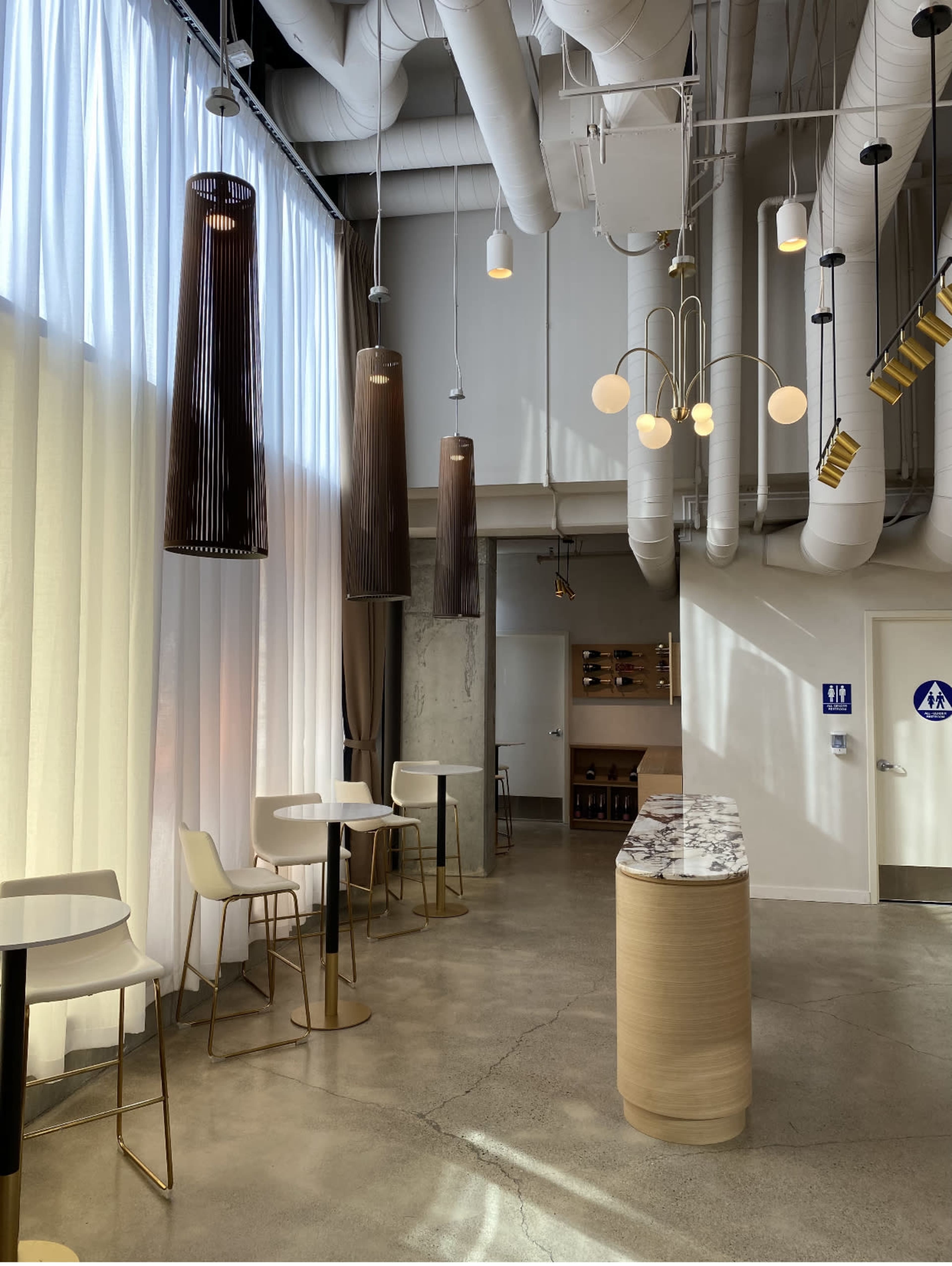 A modern cafe interior with tall ceiling, light-colored walls, and several hanging pendant lights, featuring a marble-topped counter and minimalist furniture.
