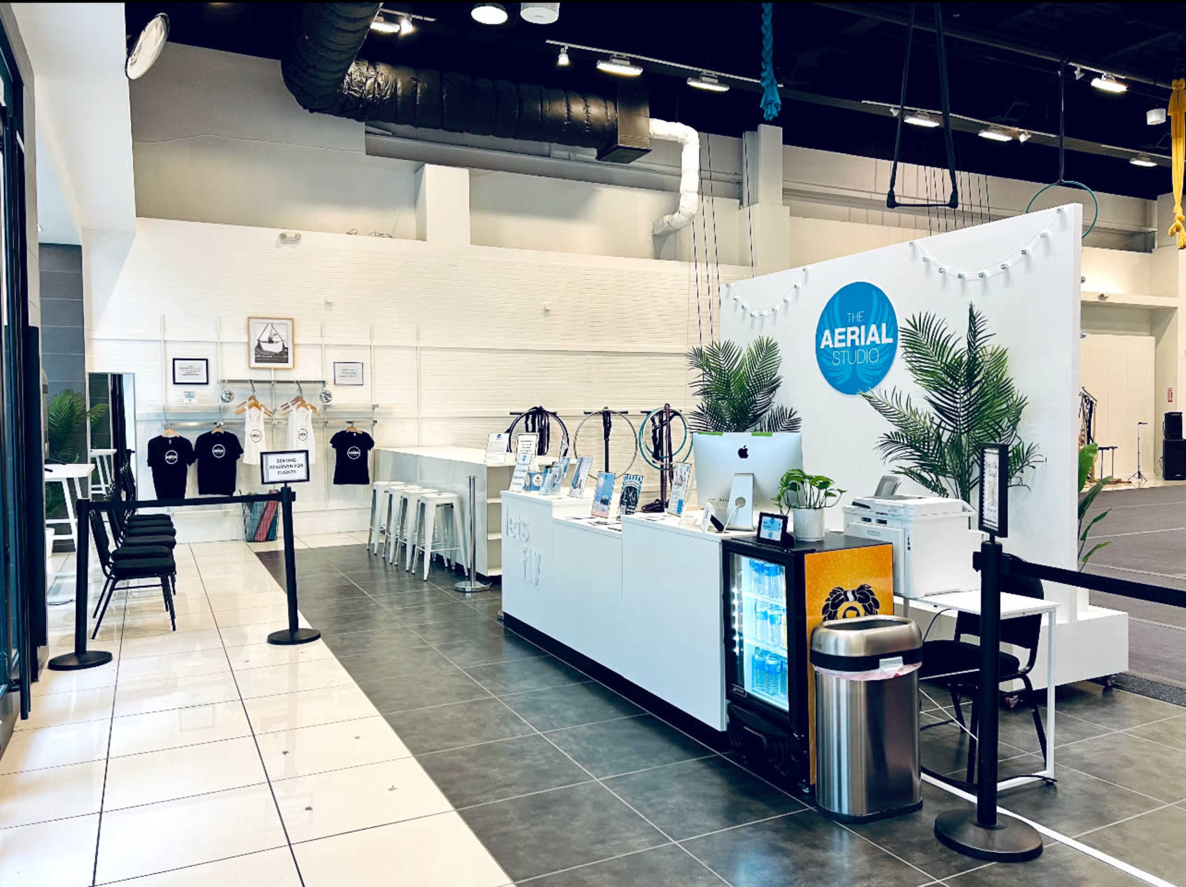 A reception area of a studio featuring a front desk, merchandise display, and seating, with a clean layout and some tropical plants.
