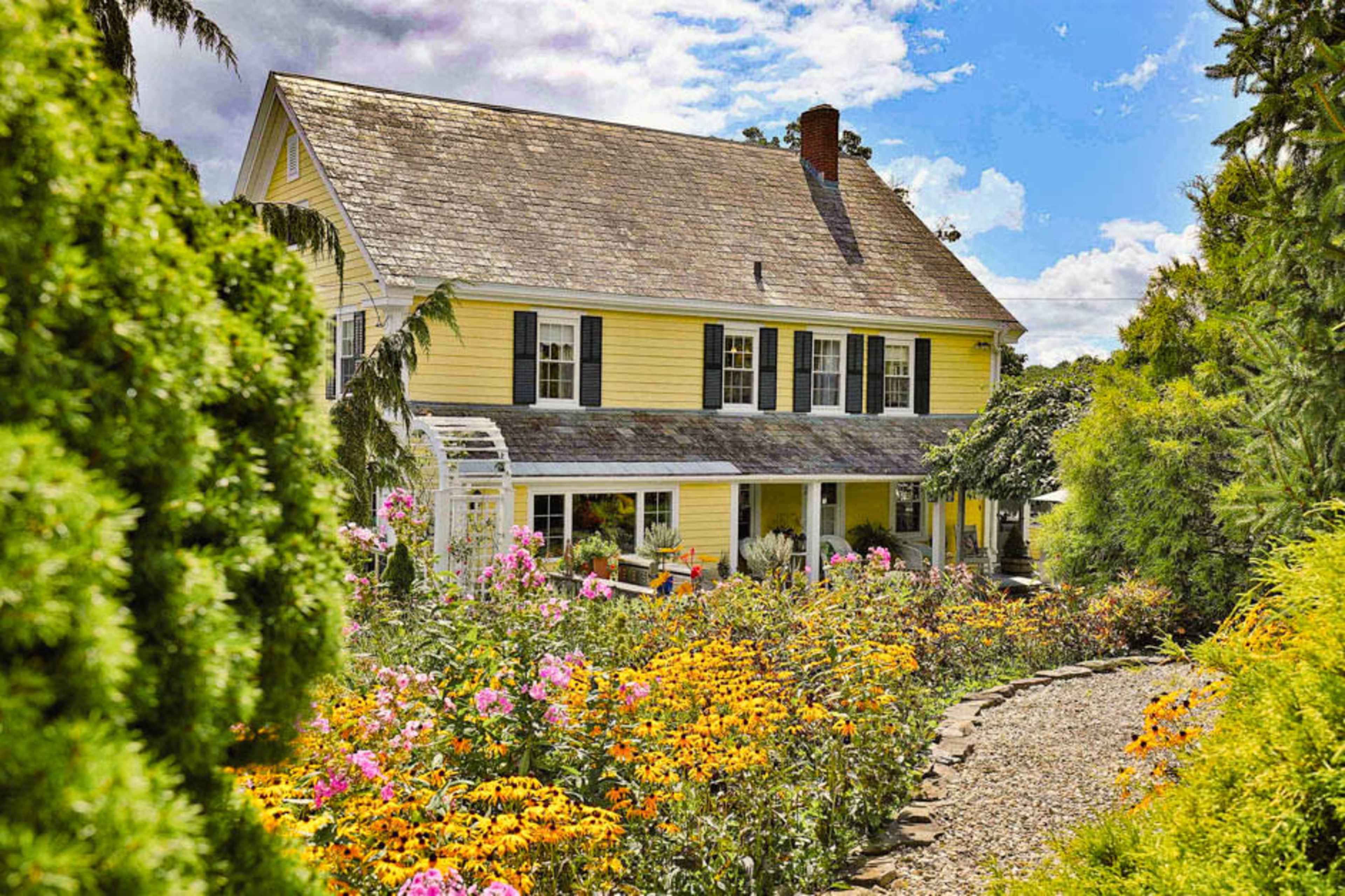 A yellow house with a gabled roof is surrounded by a vibrant flower garden filled with various colorful blooms.