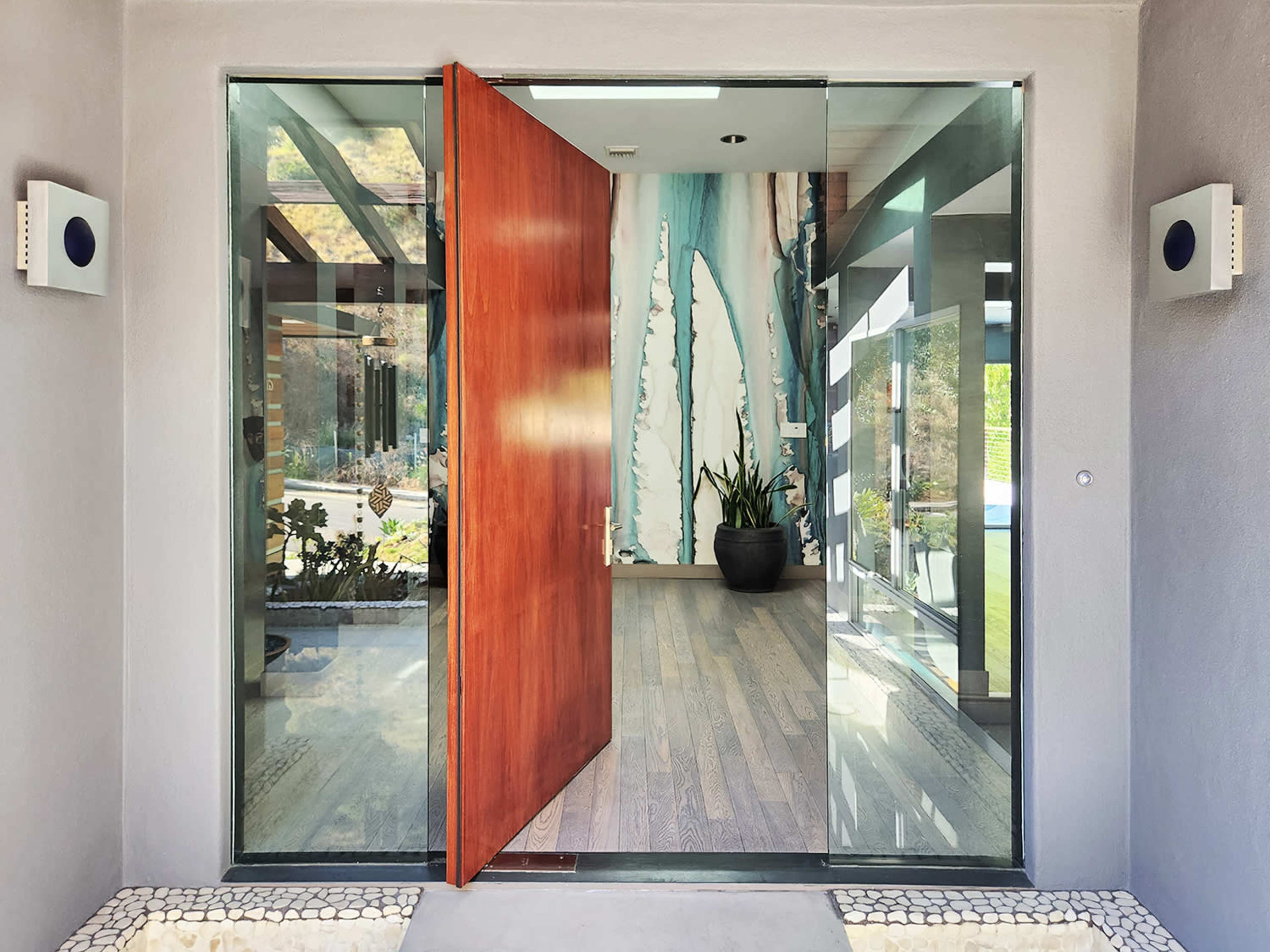 A modern entrance with a large wooden door open to reveal a hallway adorned with a decorative wall and greenery.