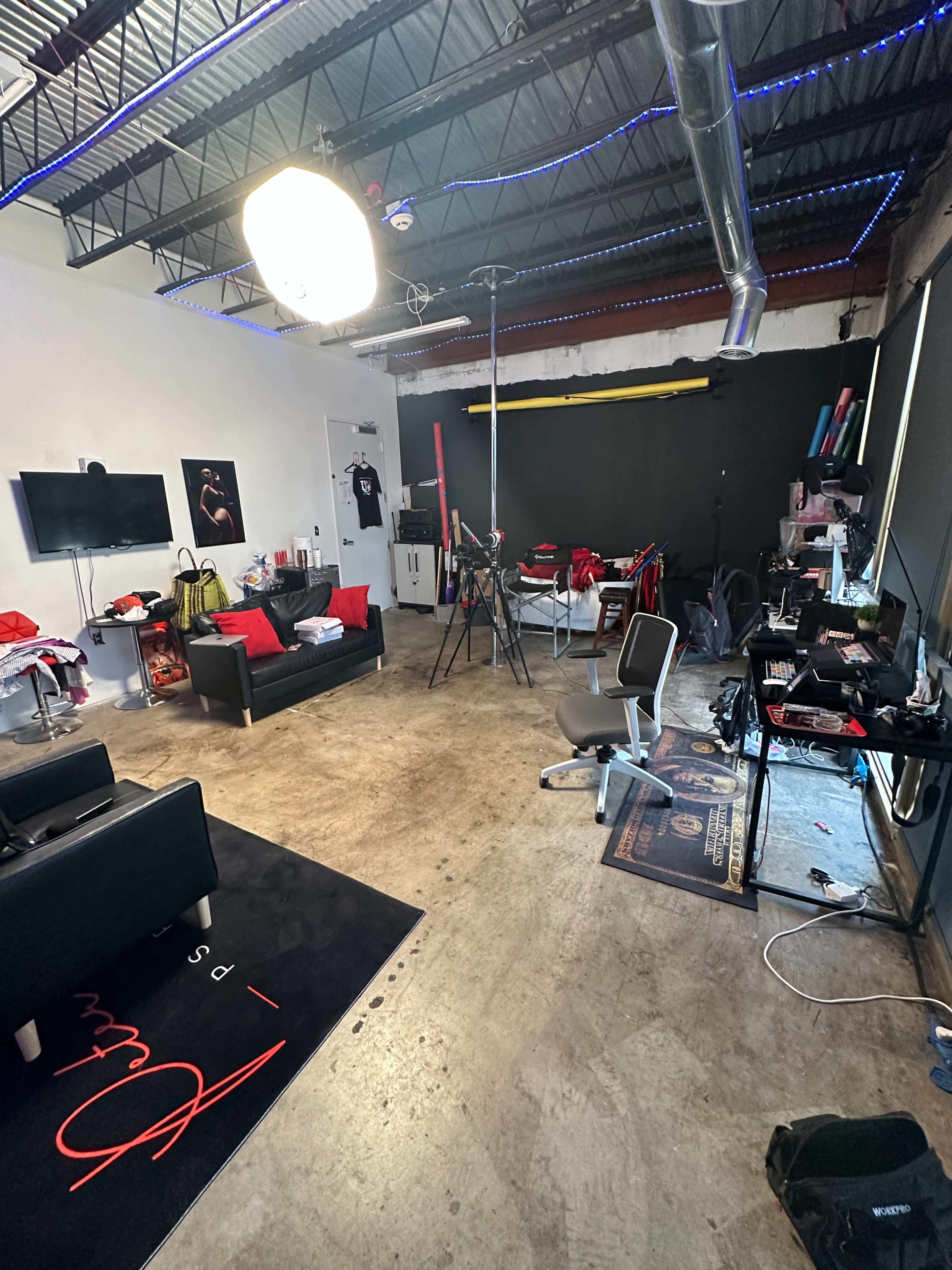 A well-lit studio space with a seating area, a television, various photography equipment, and a cluttered floor.