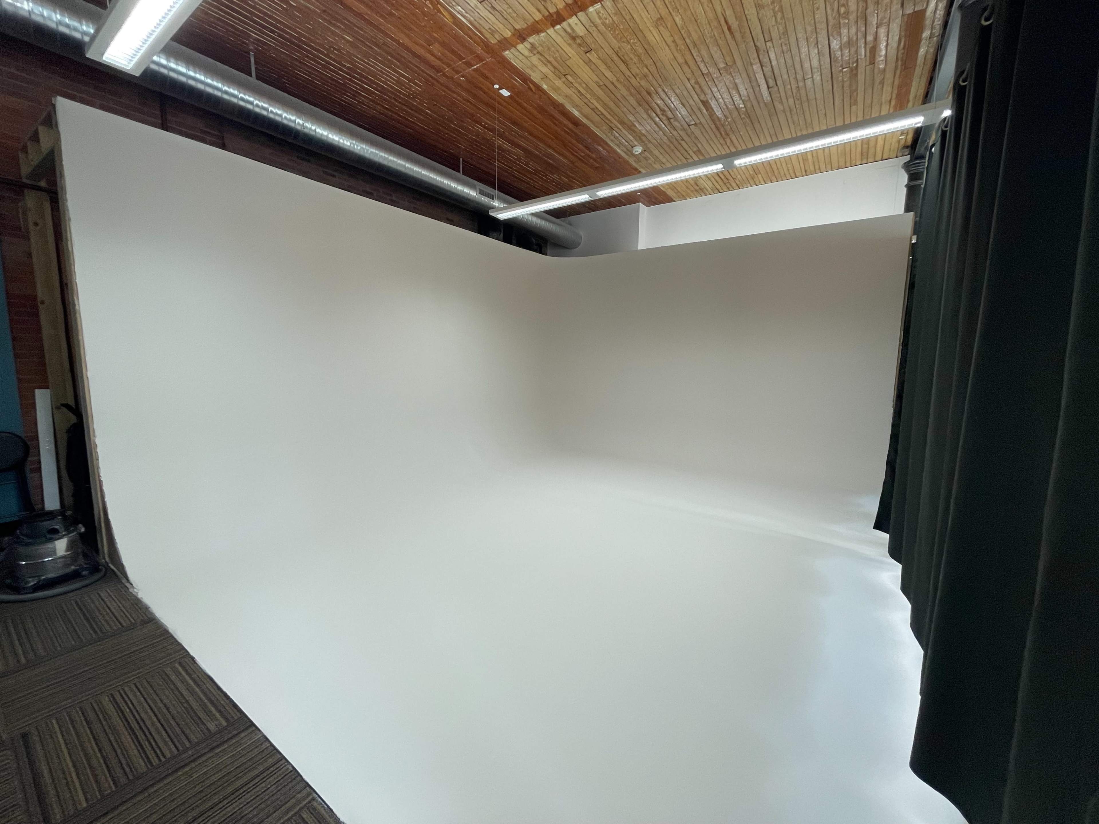 A spacious photography studio featuring a seamless white backdrop and a wooden ceiling.