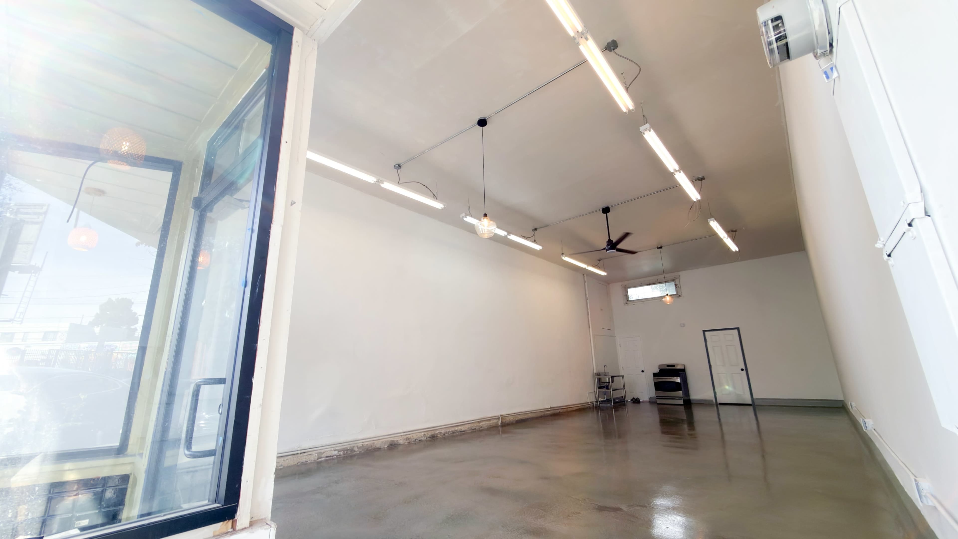 The image shows an empty room with smooth concrete flooring, bright overhead lights, and a single window offering a view outside.