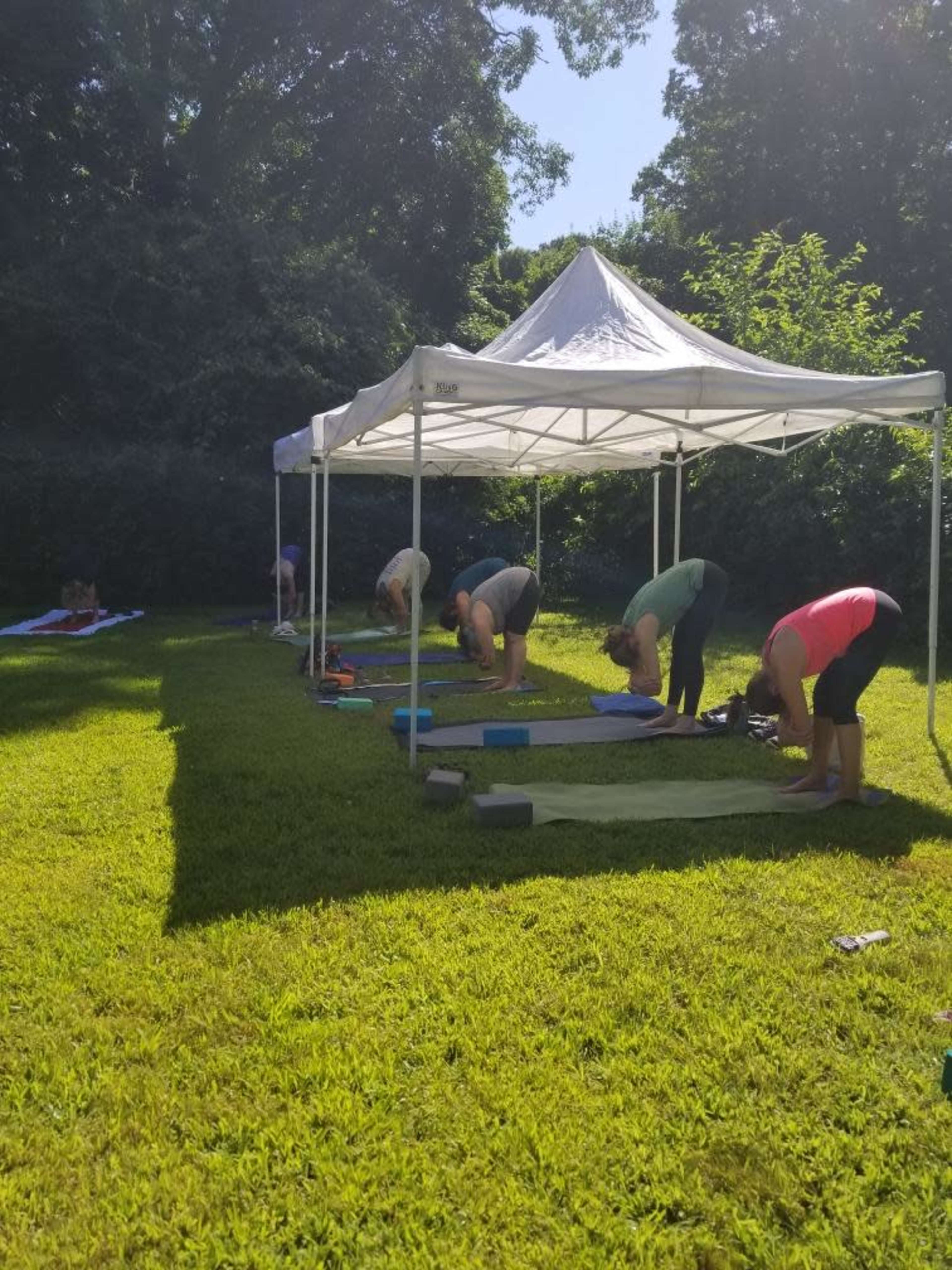 A group of people practice yoga under a white tent on a grassy area.