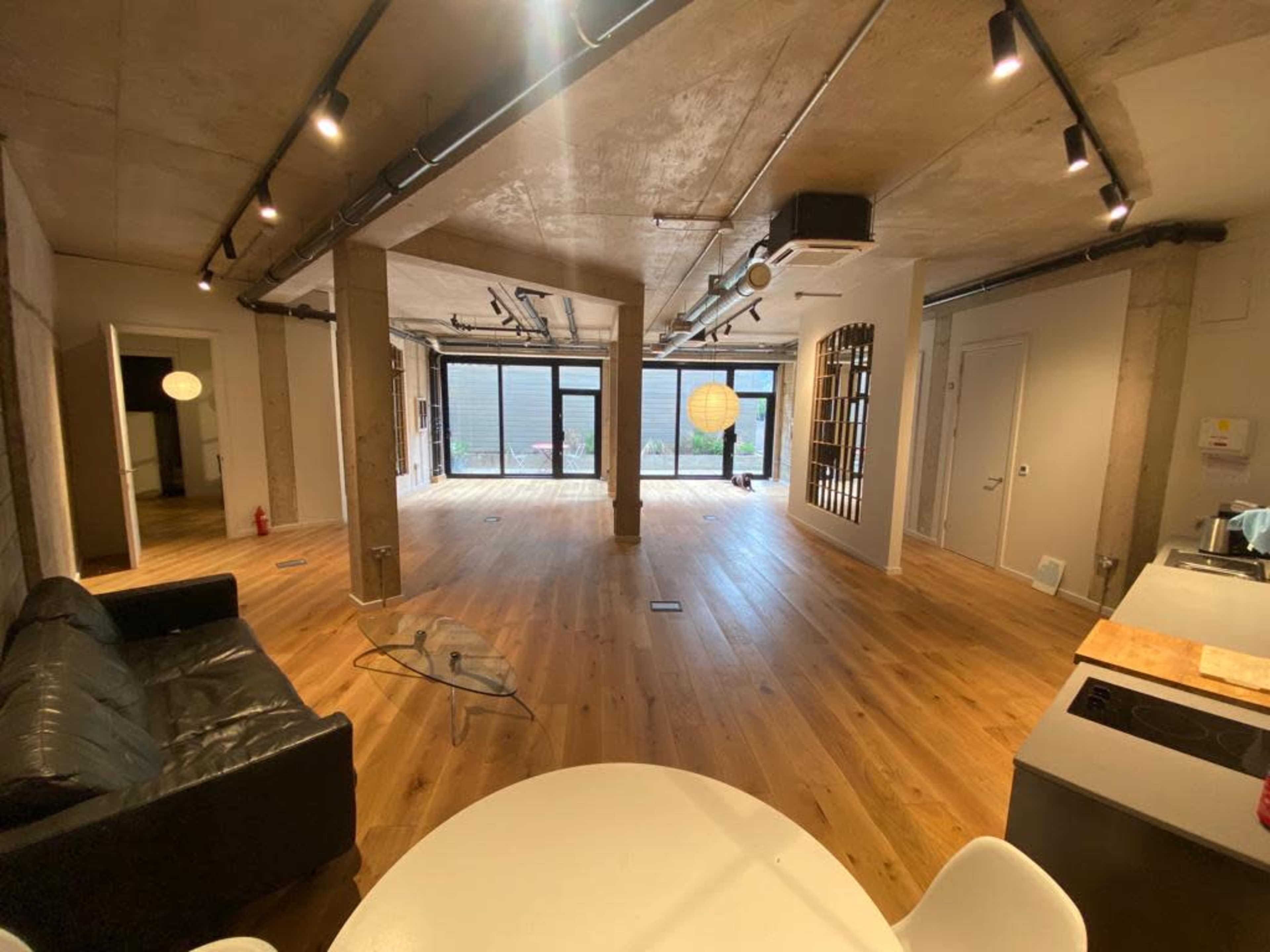 A spacious, modern interior of a room with wooden flooring, large windows, and various sections defined by walls and furniture.