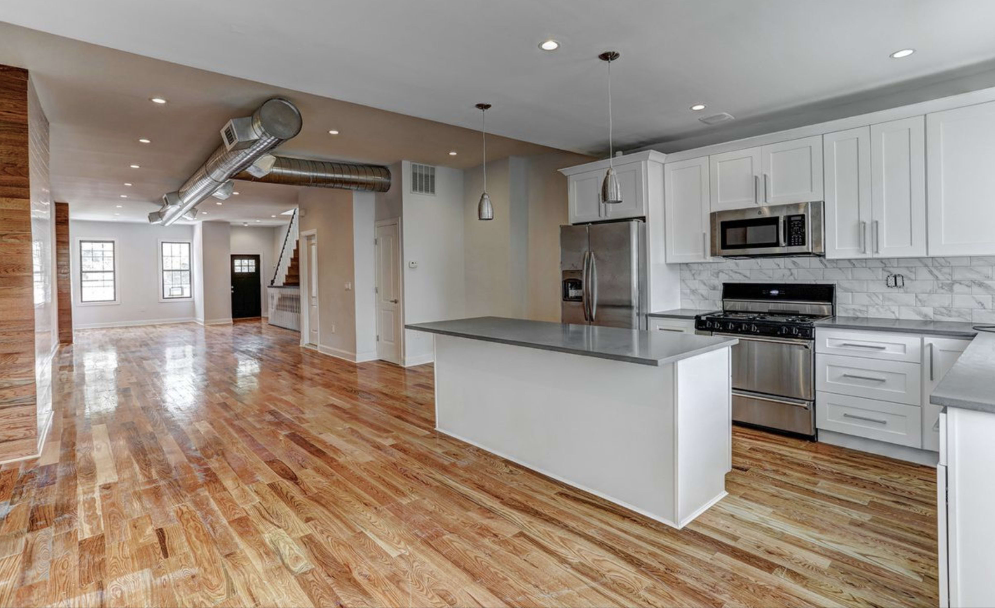 An open-concept kitchen and living area with hardwood floors, modern appliances, and an island in the center.