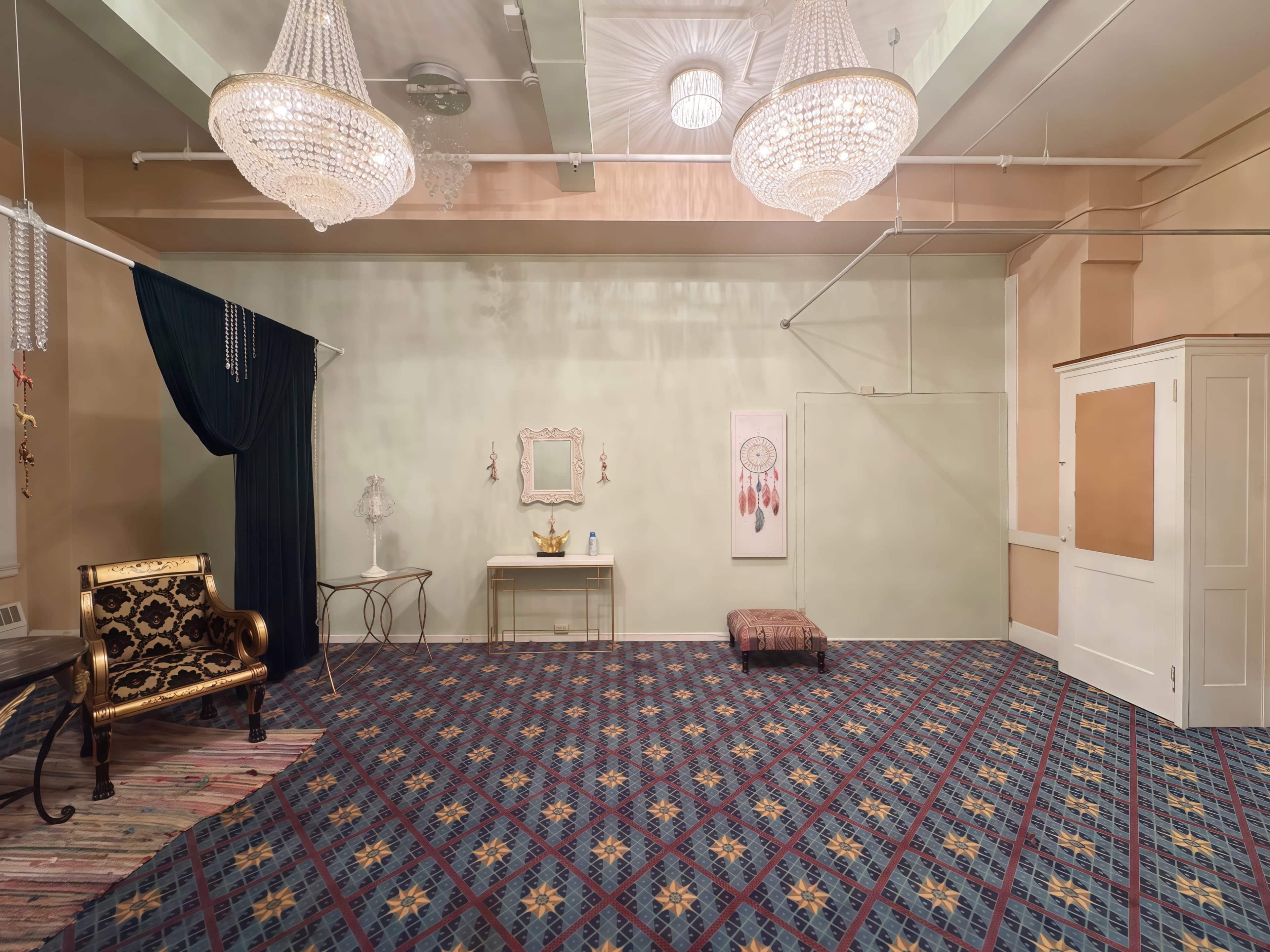 The image shows an empty room with a patterned carpet, decorative chandeliers, and various pieces of furniture including a sofa and a table.