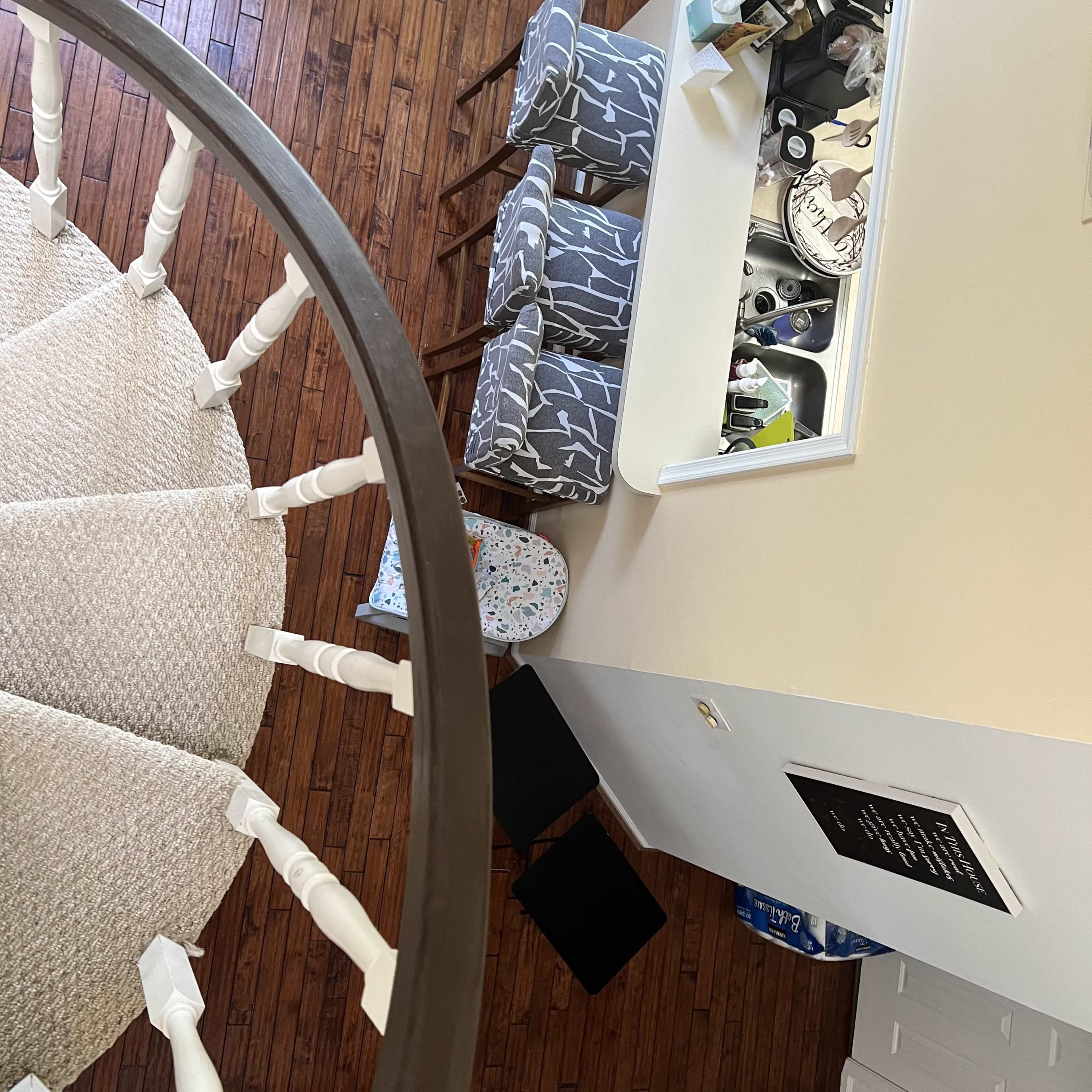 A spiral staircase leading to an open area with a counter, bar stools, and a view of the hardwood floor.