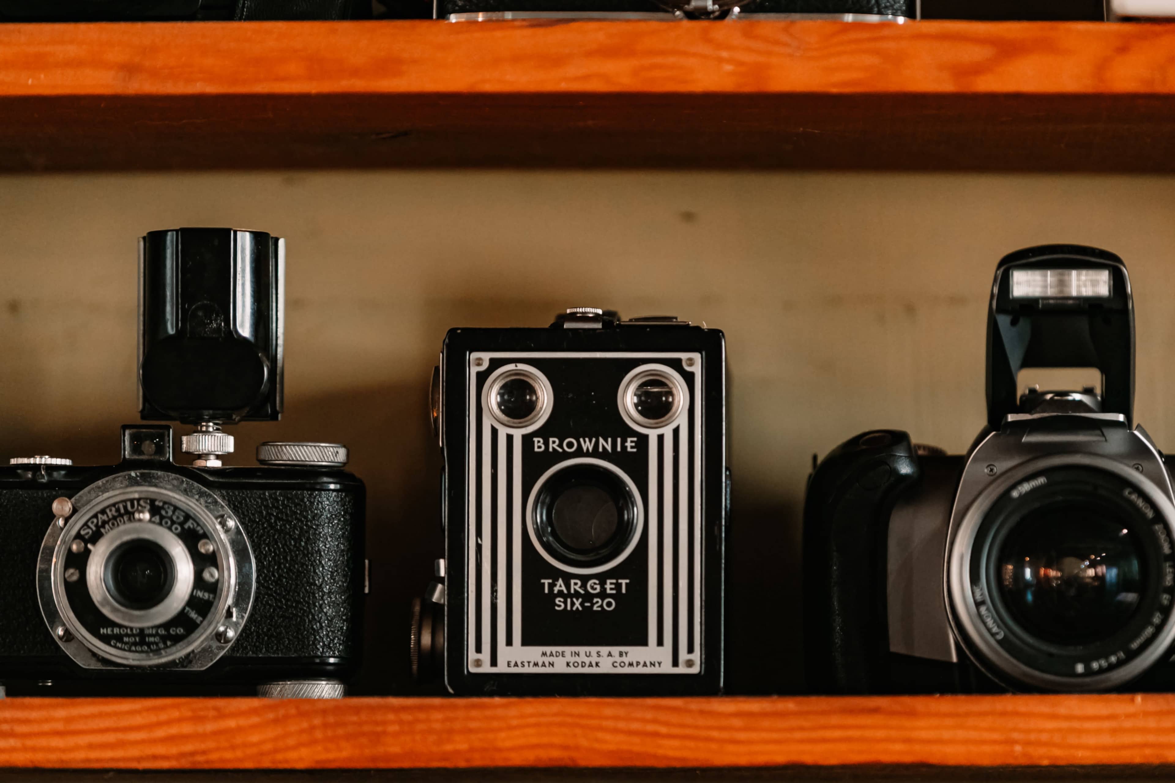 The image features a wooden shelf displaying three vintage cameras, including a Kodak Brownie Target Six-20 in the center.