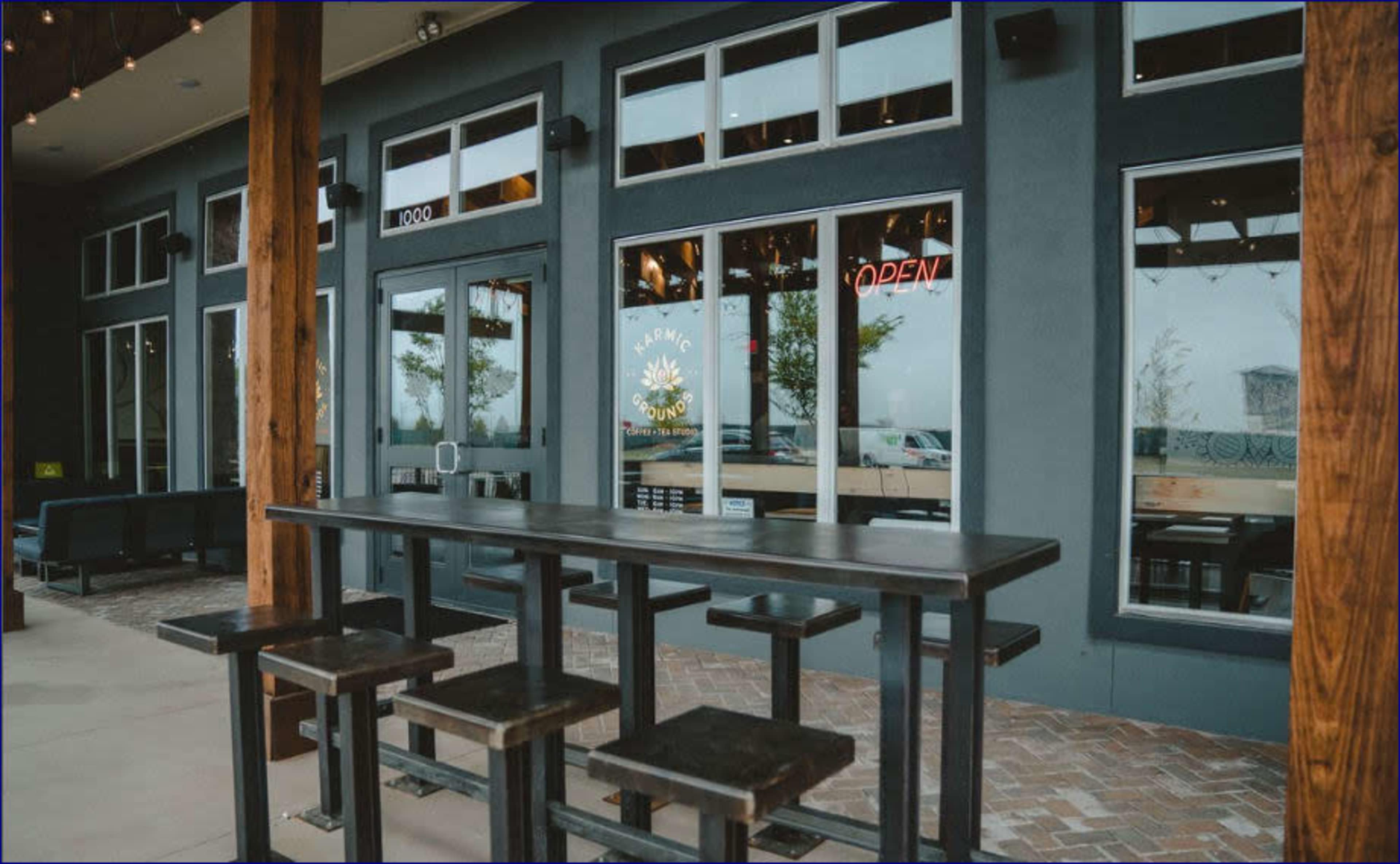The image shows an exterior view of a restaurant with large windows, a "OPEN" sign, and outdoor seating along a sidewalk.