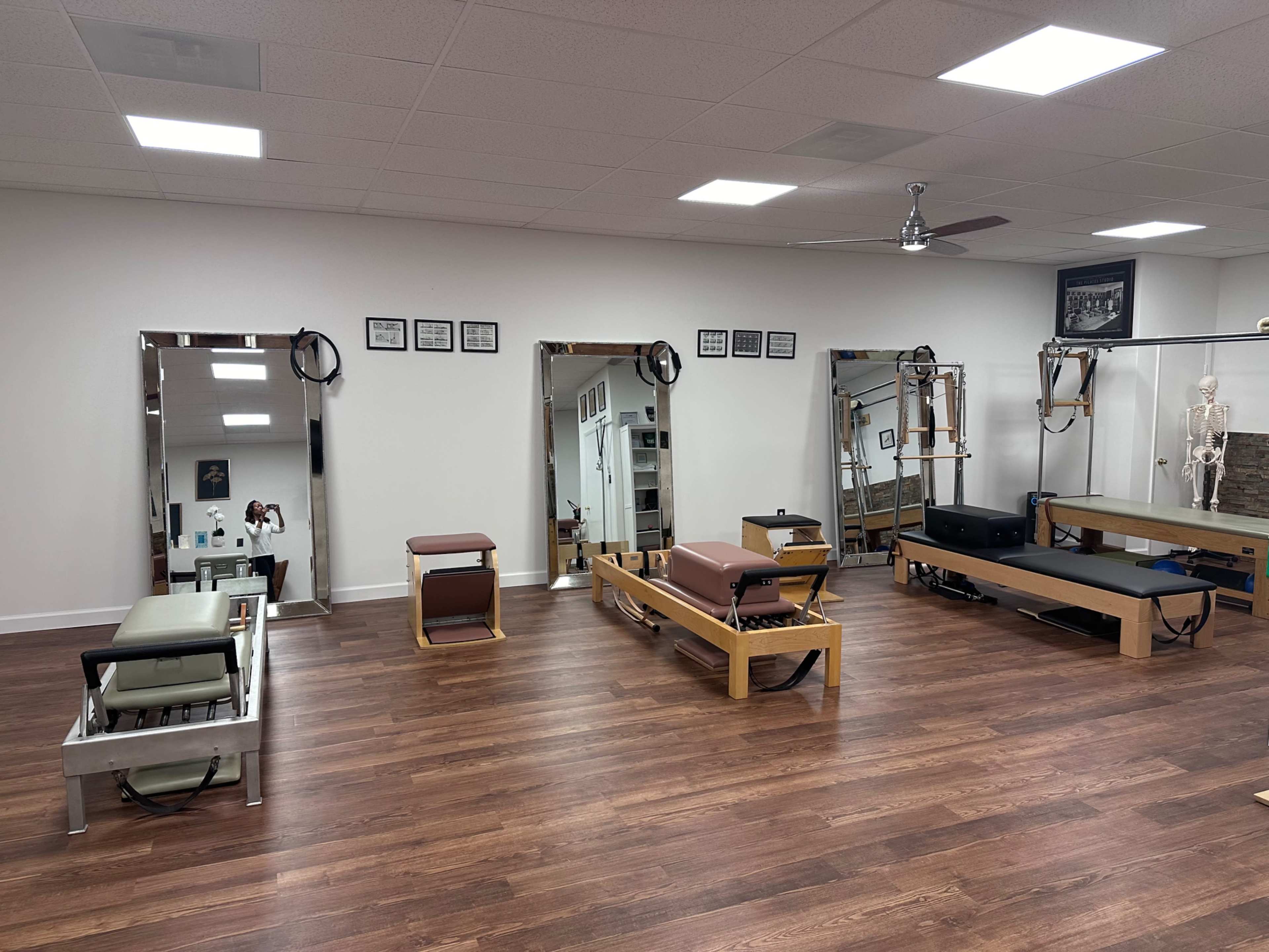 The image shows a spacious studio with exercise equipment, including reformers and mirrors, arranged neatly on a wooden floor.