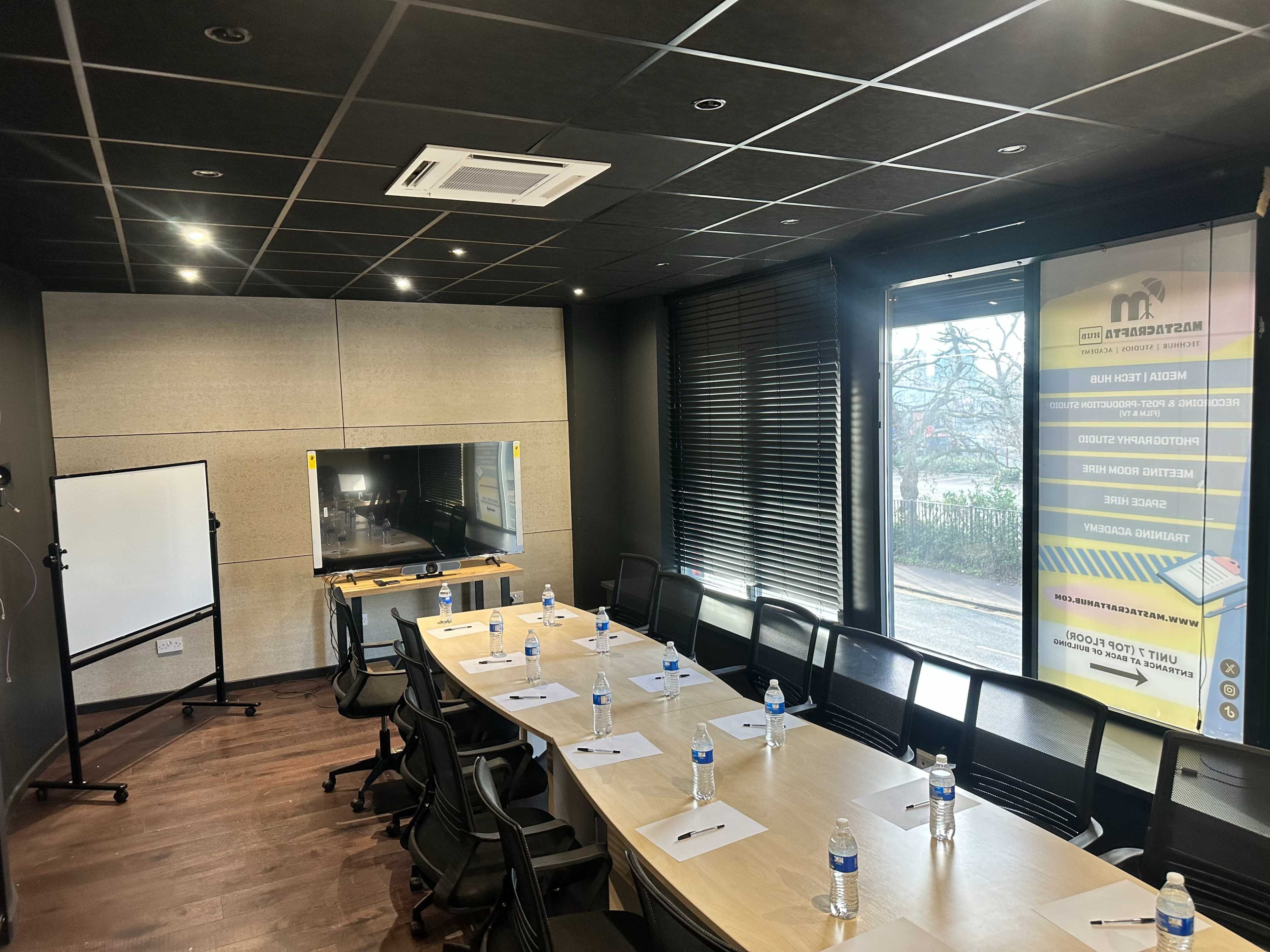 The image shows a modern conference room equipped with a large table, chairs, a whiteboard, a television screen, and bottles of water placed at each seat.