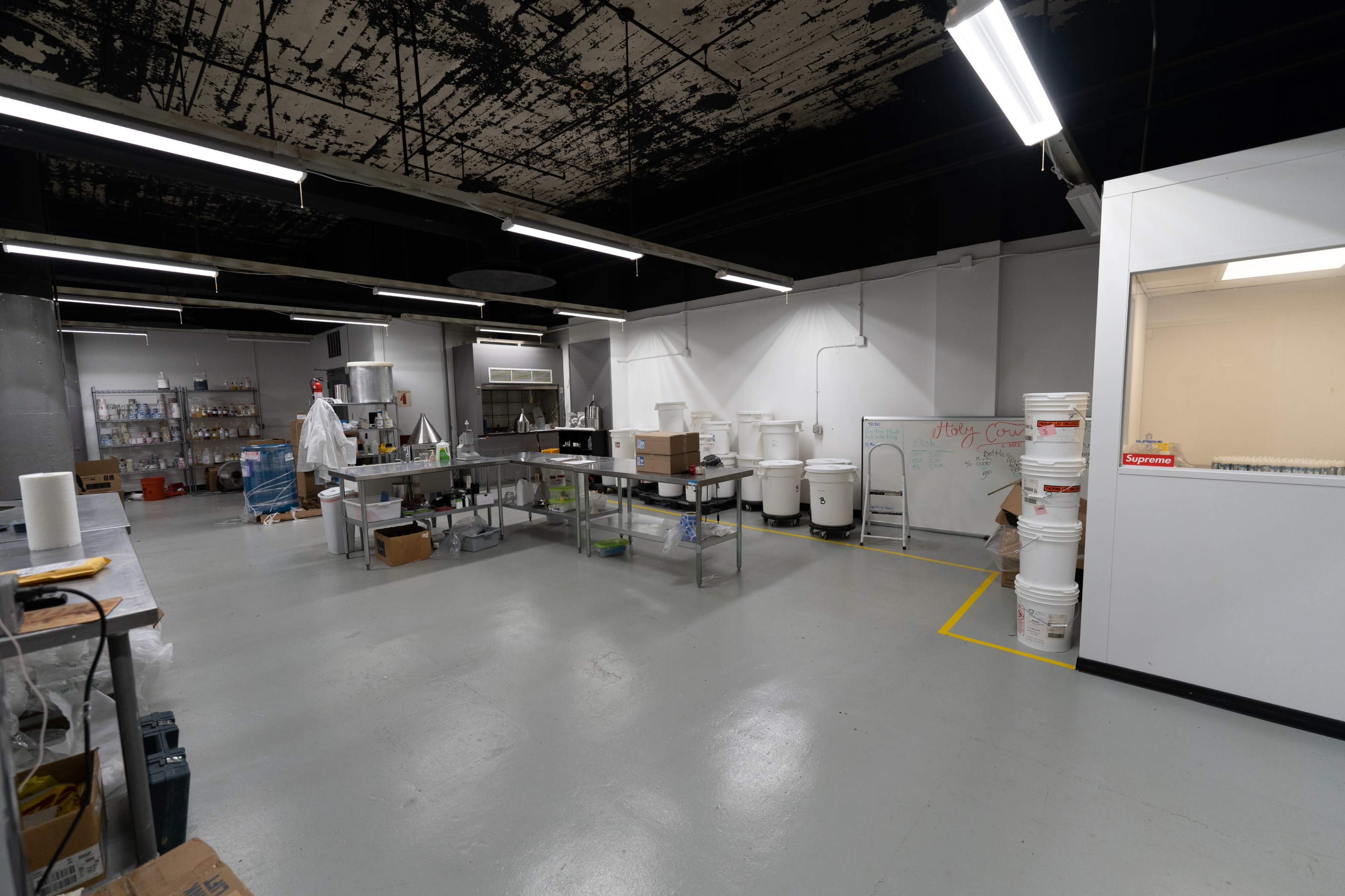 A spacious commercial kitchen features stainless steel countertops, large containers, and white walls.