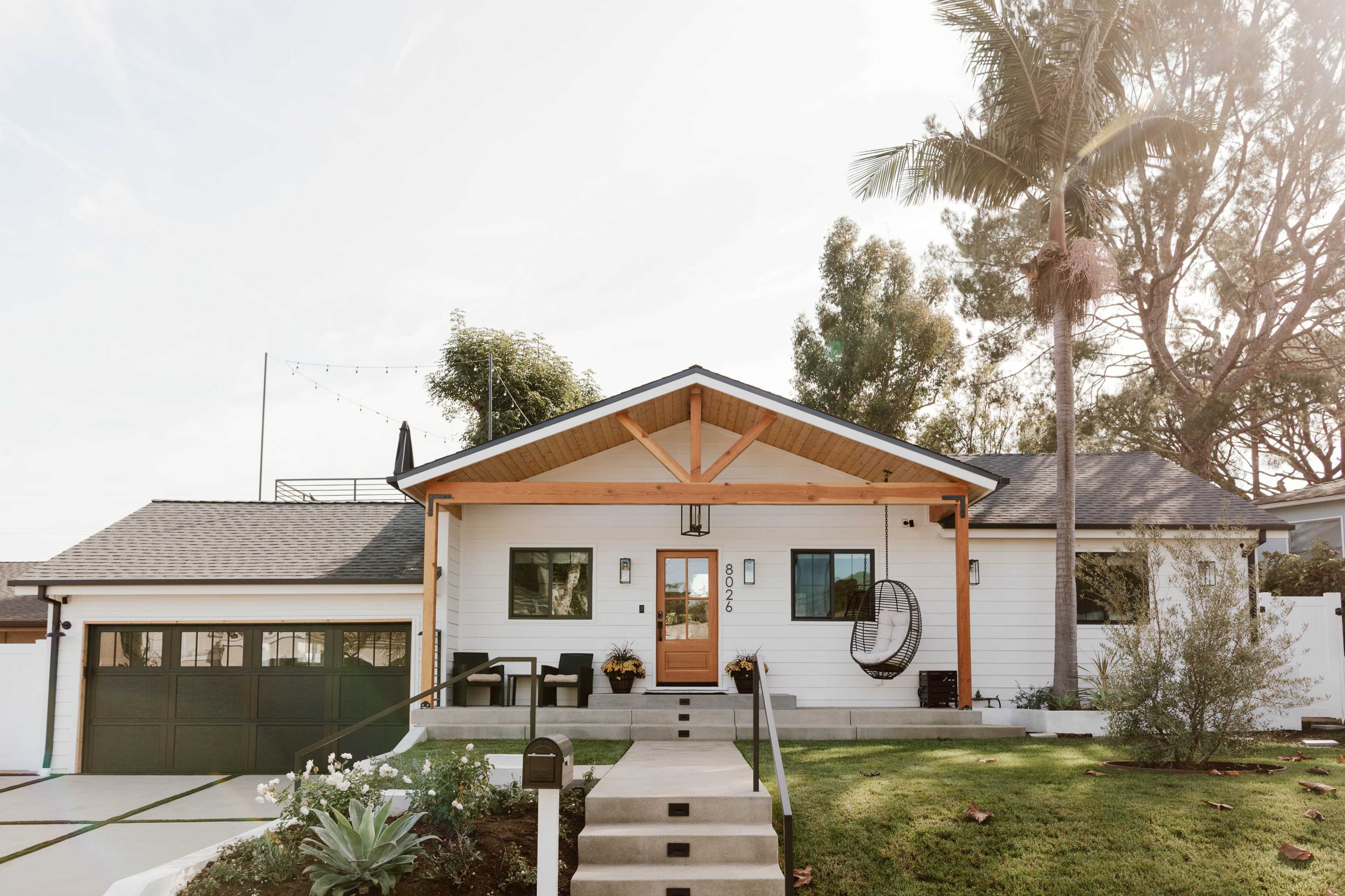 A modern single-story house with a wooden porch, palm trees, and a manicured lawn.